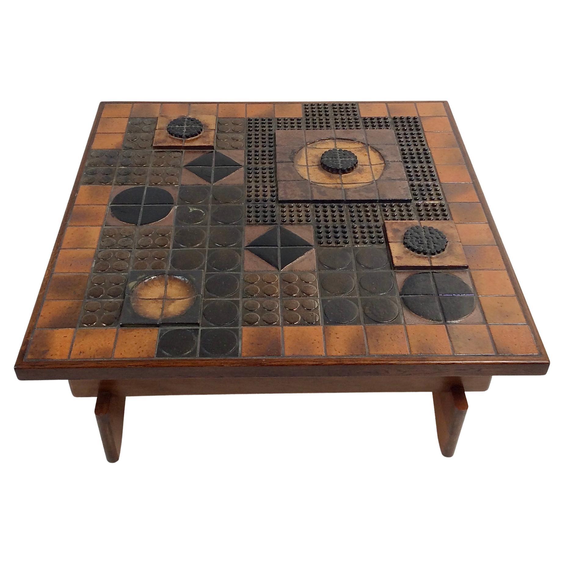 Impressive ceramic square coffee table circa 1960, France.
In the style of Roger Capron, glazed ceramic tiles in shades of tan, yellow, black, orange, brown.
A succession of recessed and protruding ceramic parts intensifies the effect of