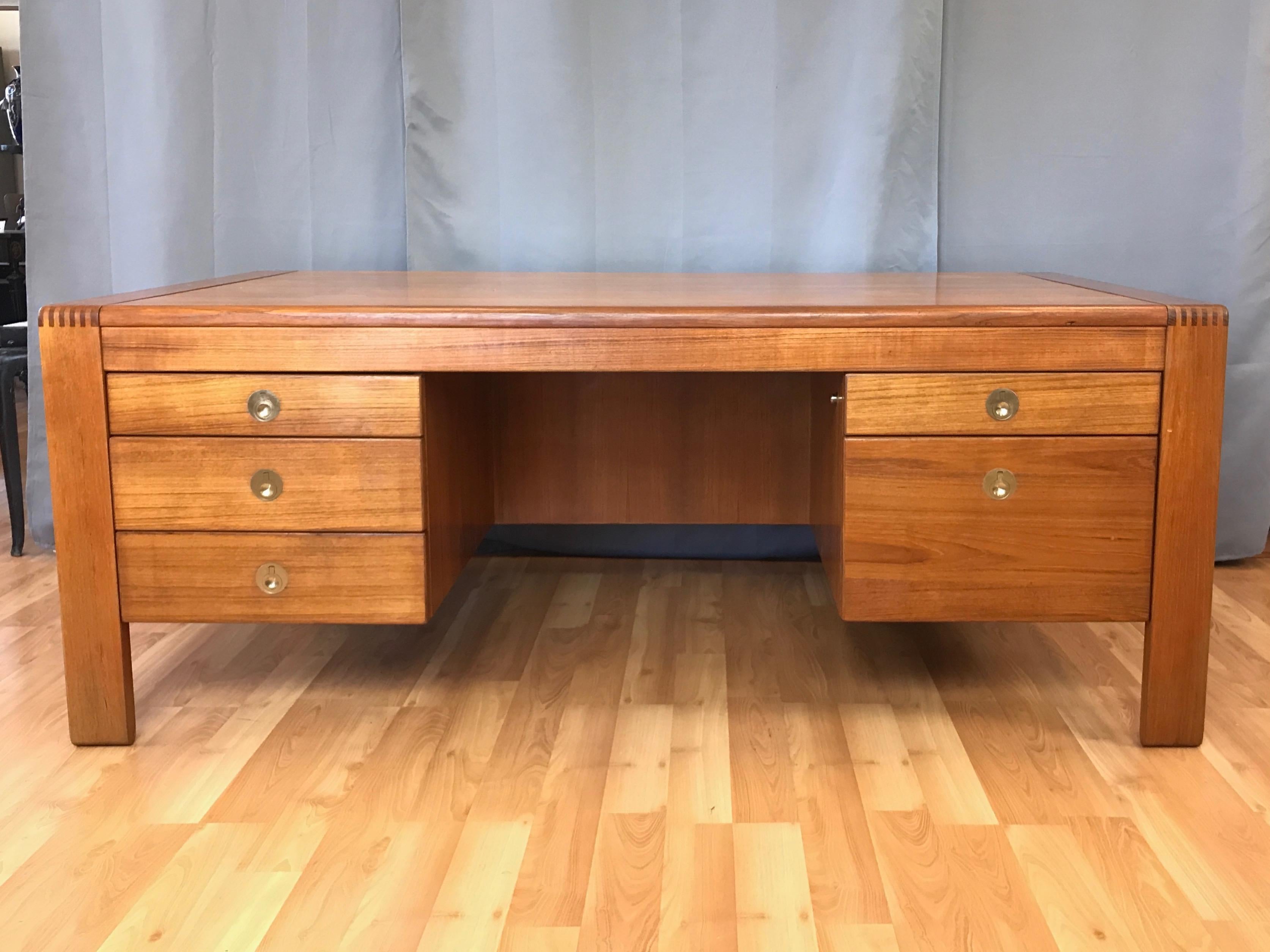 A large, well-crafted, and impressive 1970s teak executive desk by D-Scan.

Clean Danish modern-inspired design distinguished by 3.75” wide solid teak legs with exposed finger joinery in the style of Niels Bach or Peter Hvidt. Expansive top