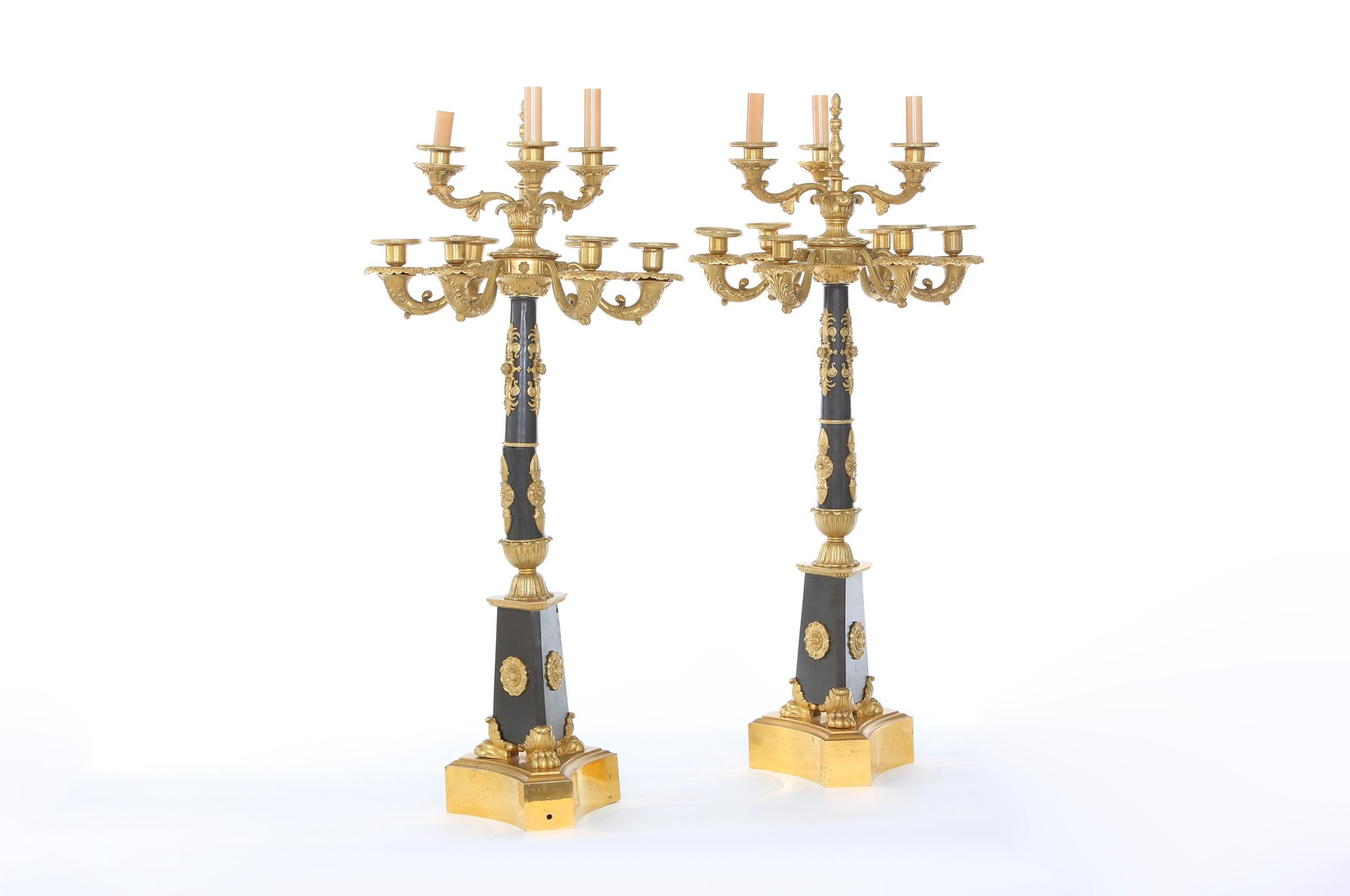 Impressive French Empire style gilt bronze nine-light torchieres / candelabras with exterior design details raised on a tripart concave plinth. The torchiere is in great condition. Minor wear consistent with age / use. Each one stand about 36 inches