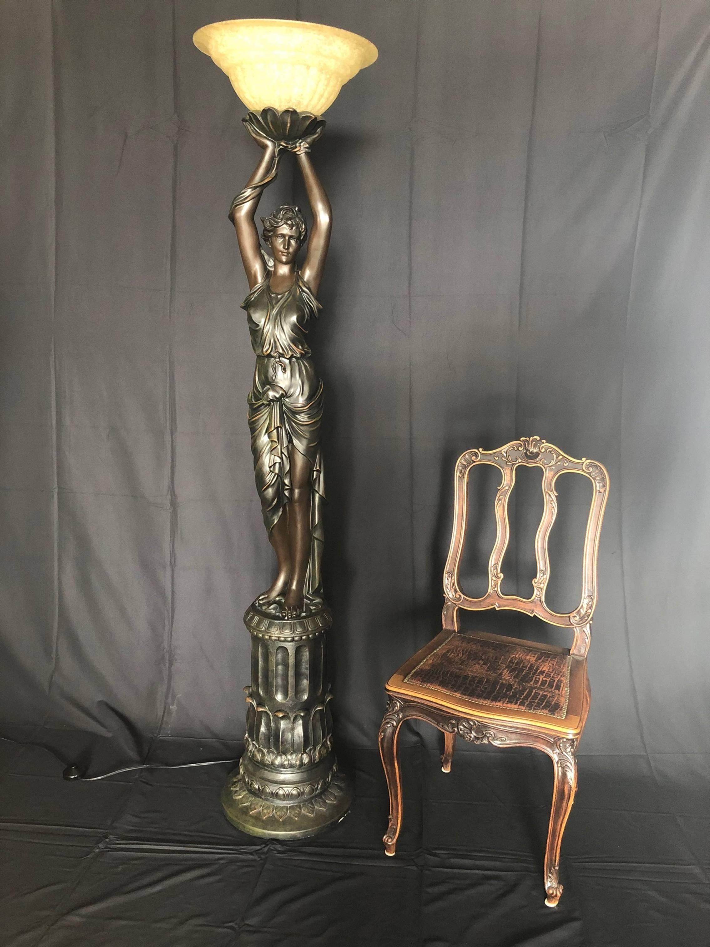 A beautiful figurative patinated floor lamp of impressive size having an Art Deco style woman holding up a light, supported on a raised round reeded pedestal base. Both of her hands hold a torch raised above her head, its handle fluted and carved