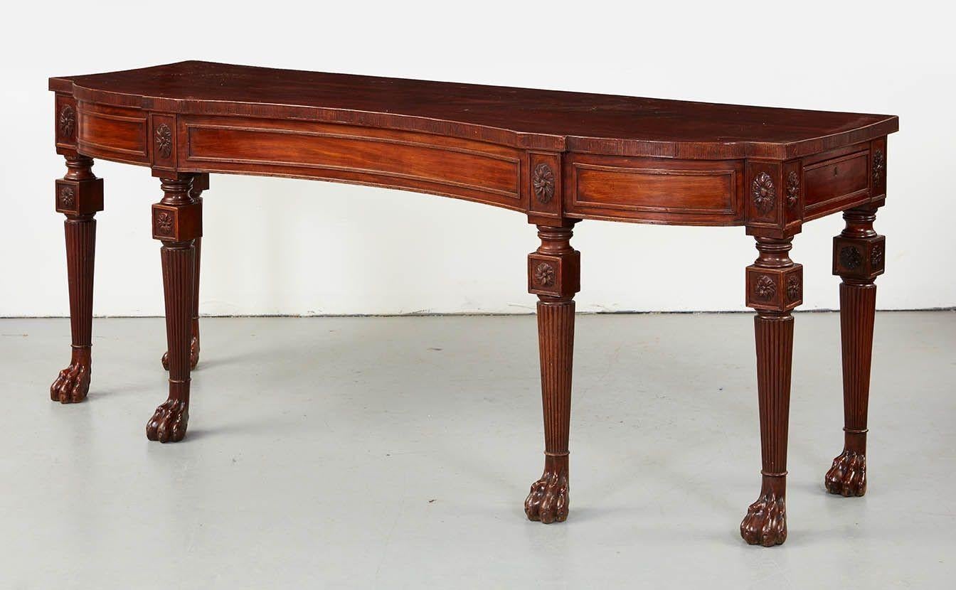 Fine and impressively scaled Irish Regency mahogany hall table, the concave shaped top with ribbed edge over paneled apron with end drawers, and having carved patera over turned and ribbed legs ending in collared paw feet, the whole possessing good
