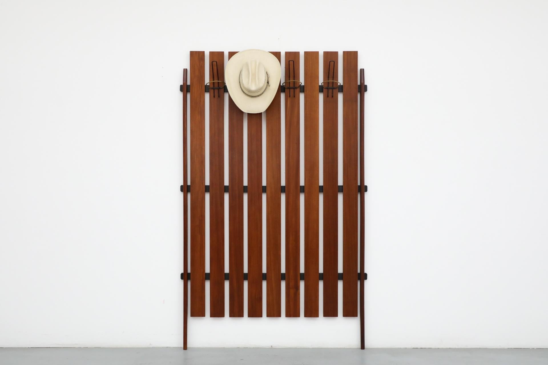 Grand porte-manteau mural italien en teck à lattes verticales avec 4 grands crochets en fil de fer en laiton et émaillé noir et des supports extérieurs en teck massif sculpté de façon organique. En bon état d'origine avec une légère retouche,