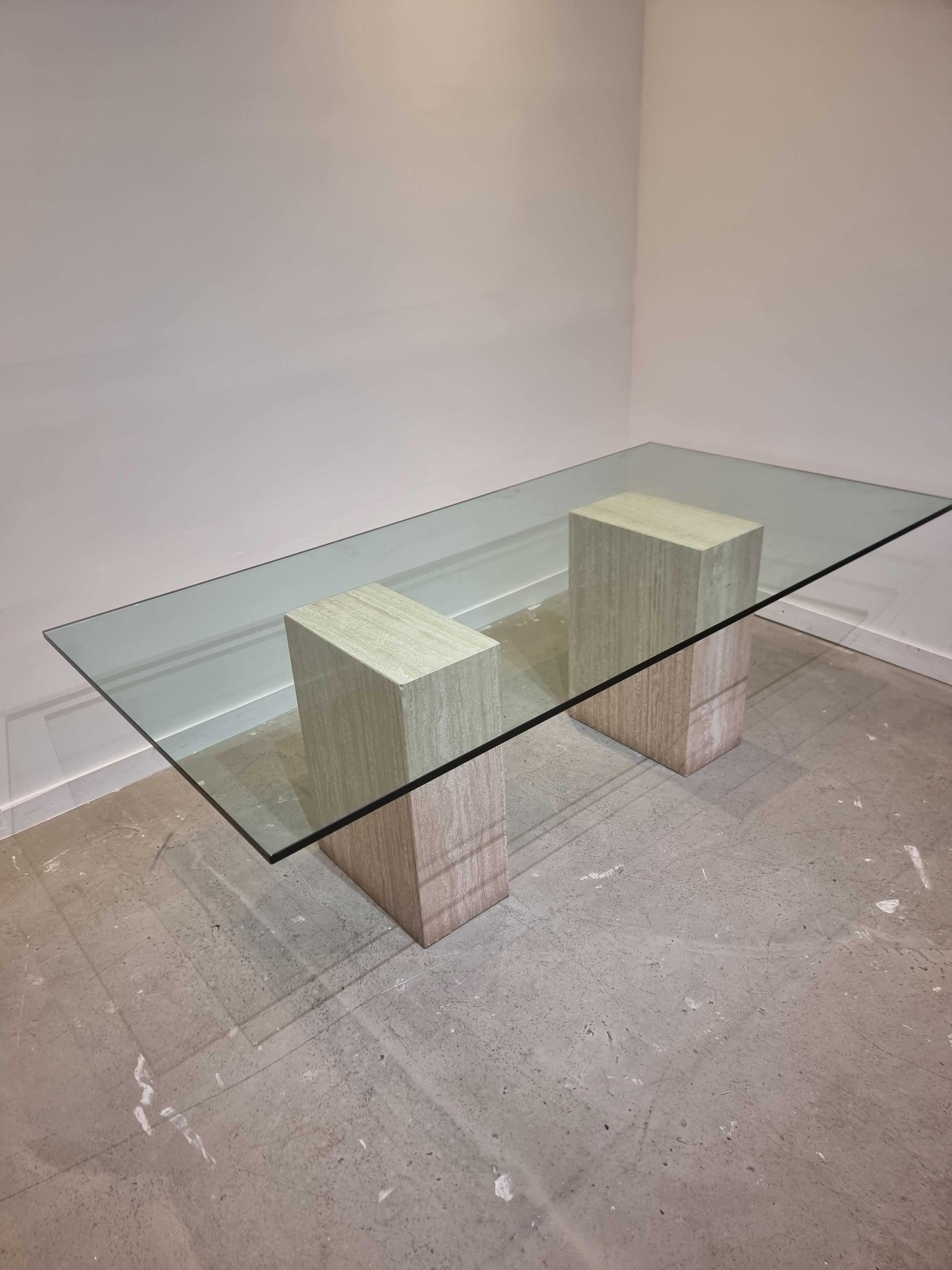 Postmodern piece in travertine marble that can be used as a writing desk or dining table. Fits 6 to 8 persons.

The two impressive travertine columns are not attached to the thick glass tabletop, these can be placed freely underneath the top. 

In