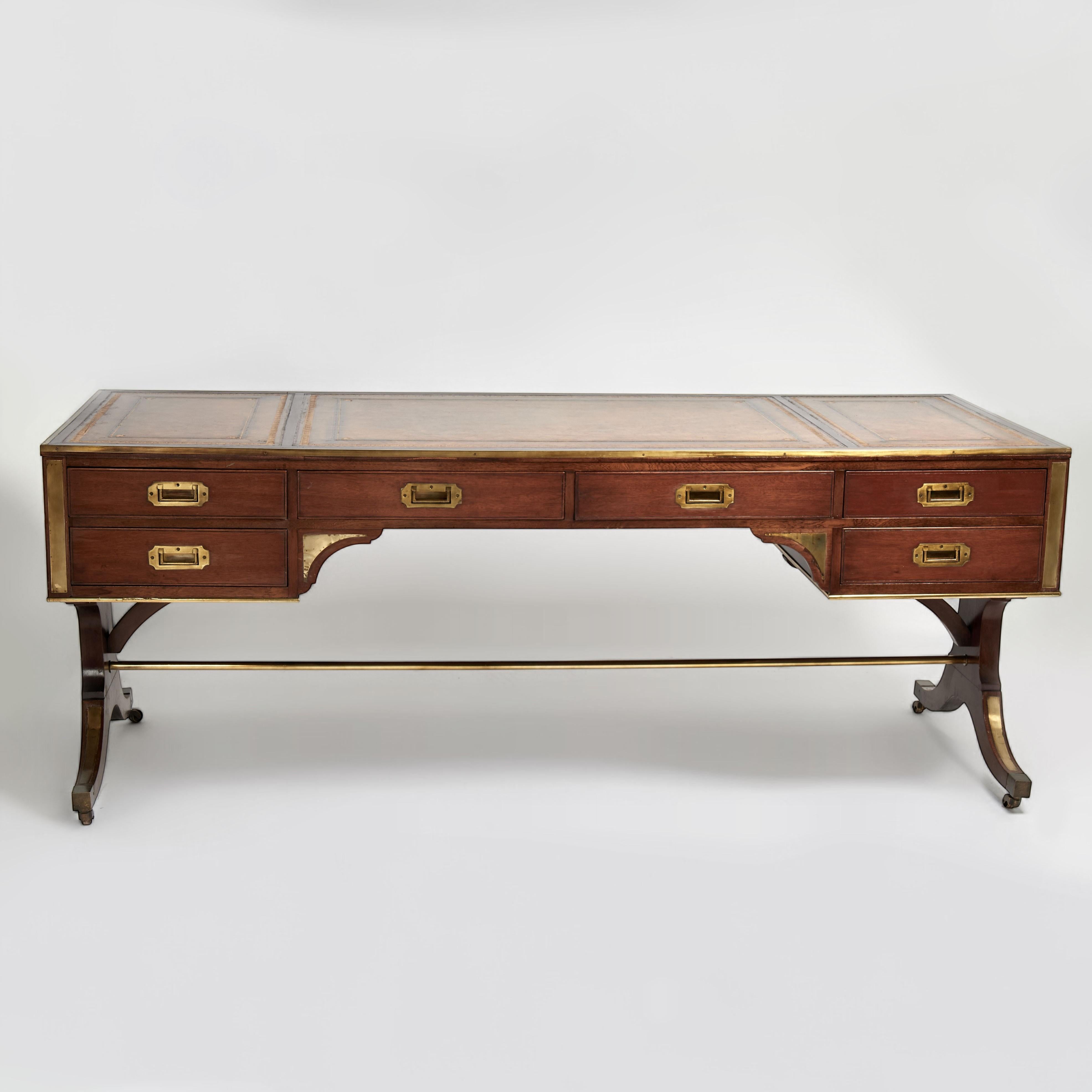 Impressive large antique Regency Style  English desk with brass campaign hardware, crafted in mahogany with a three tooled leather panel top over a trestle base on brass casters; case with six frontal operating drawers and six faux drawers on the