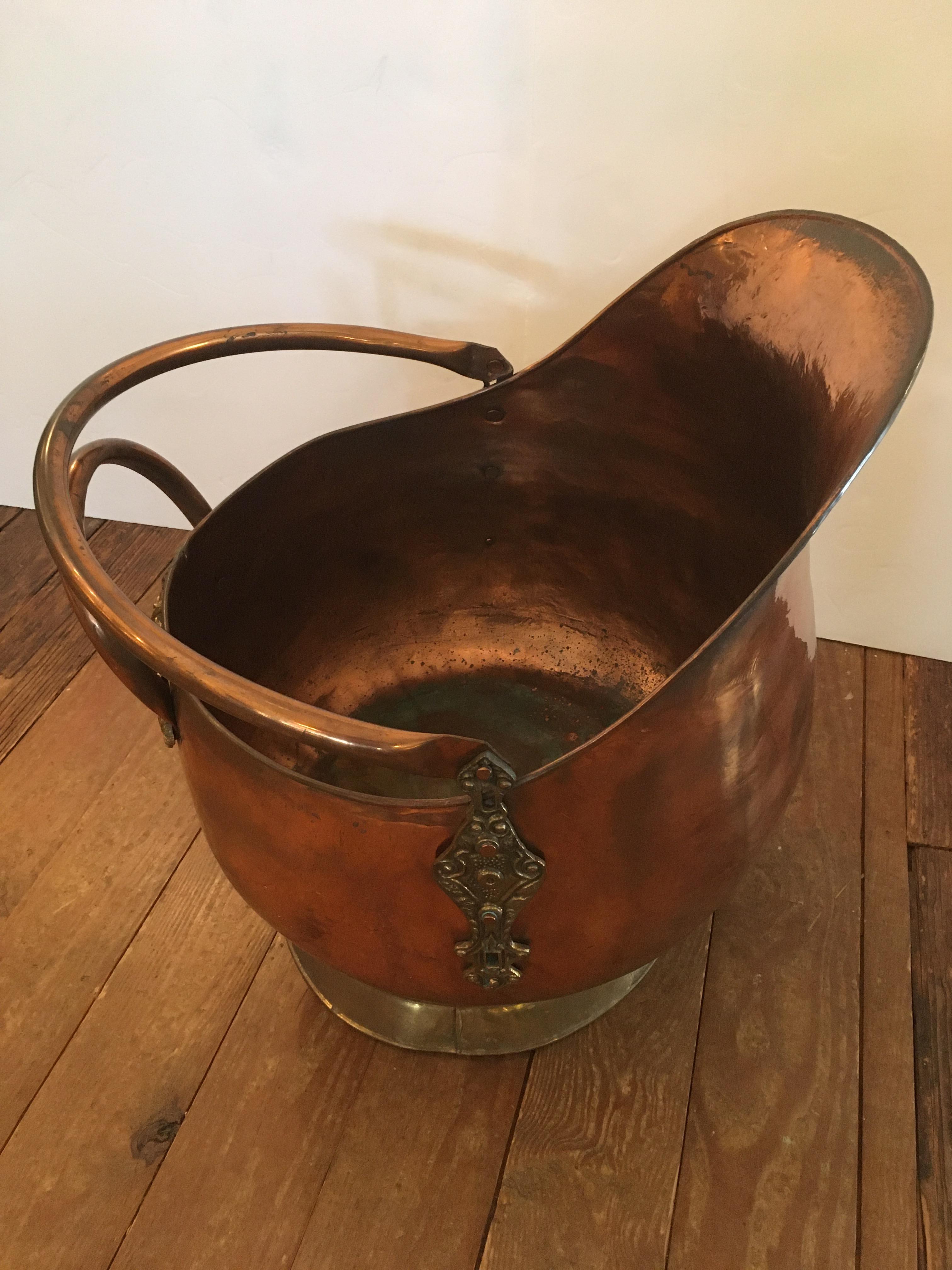 A large impressive antique copper coal scuttle having decorative brass base and hinges with wonderful pitcher shape. Would be beautiful as a magazine or kindling holder.