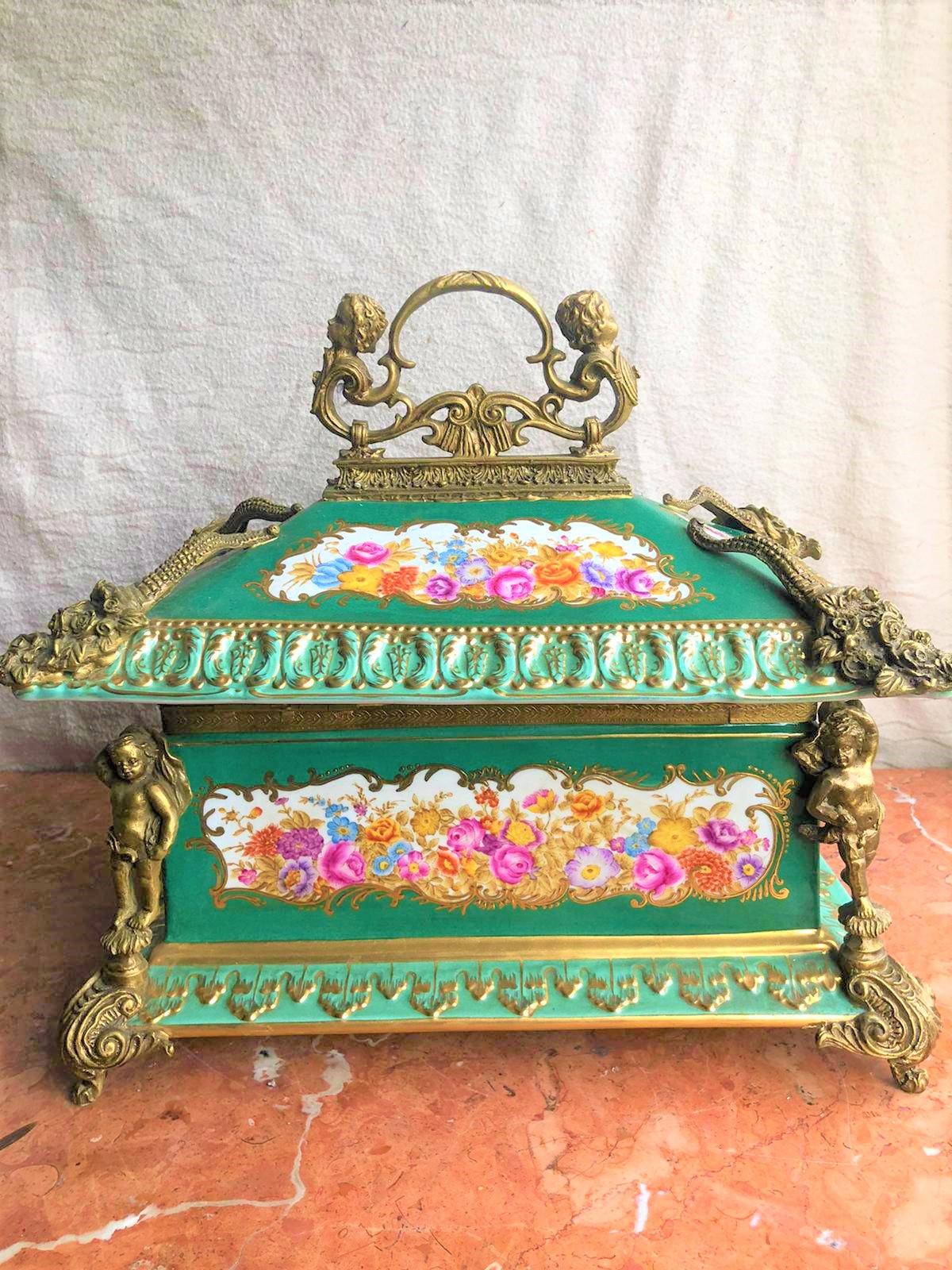 An large emerald green colored Sevres style gilded bronze jewelry box with scenes of nature and painted flowers. Decorated with bronze and painted with bouquet of flowers and cherubs on each corner laying on imperial stands. Accompanied with