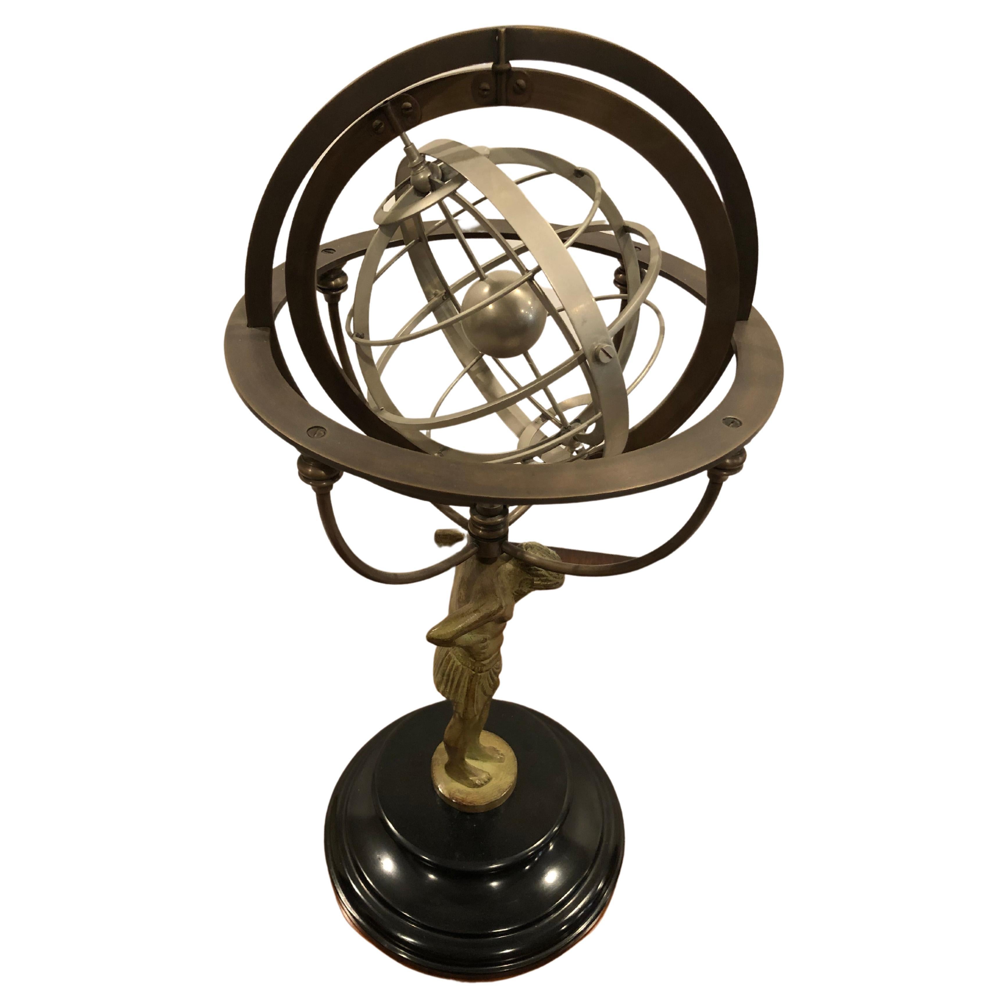 Impressive armillary sculpture in grey cast metal of a half clothed muscular man holding a round globe form on his shoulders. The round structure has a central solid ball and multiple open circular forms surrounding it. Round base is solid black.