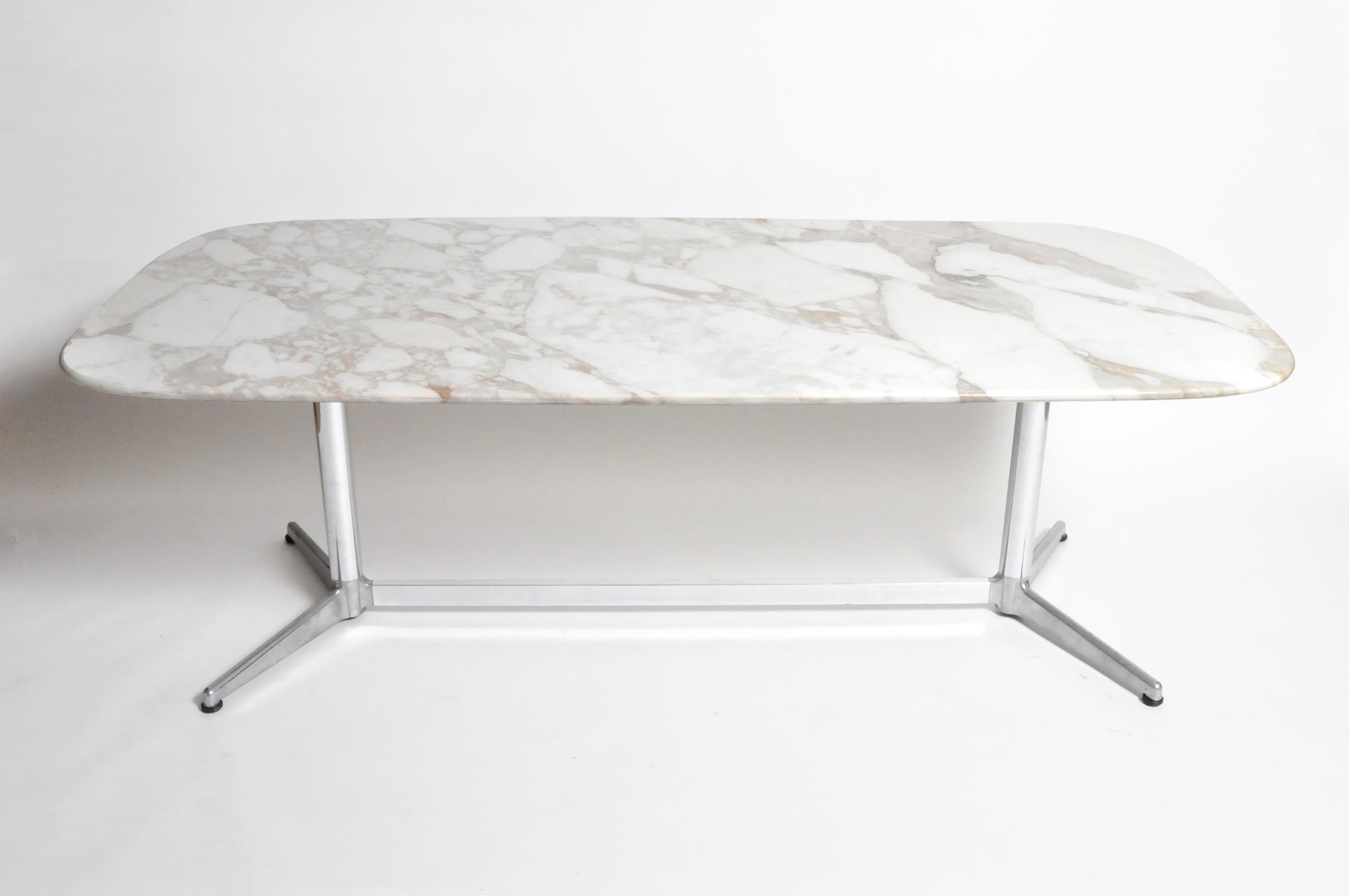 This modern marvel’s stunning oval top is made from a single slab of white stone with grey, gold, and brown veining. The remarkably thin tabletop is raised on a pair of cylindrical chrome-plated pedestal legs, each with two feet, joined by a long