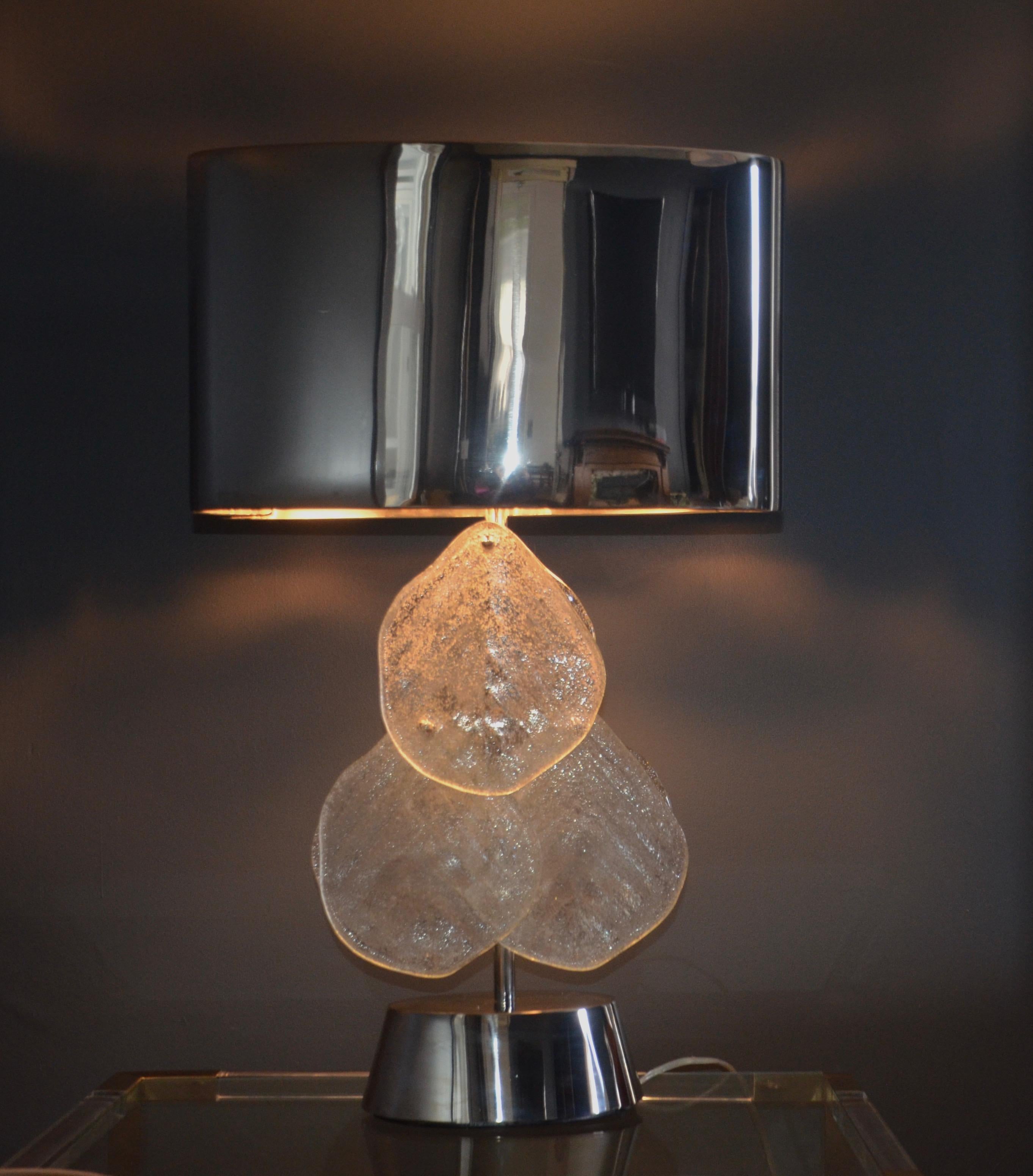 This contemporary lamp is composed of a chrome base, body, and shade with attached Murano glass petals. The petals have a textural appearance and mimic the look of a leaf. While the base of the lamp is contemporary this shade might be a marriage as