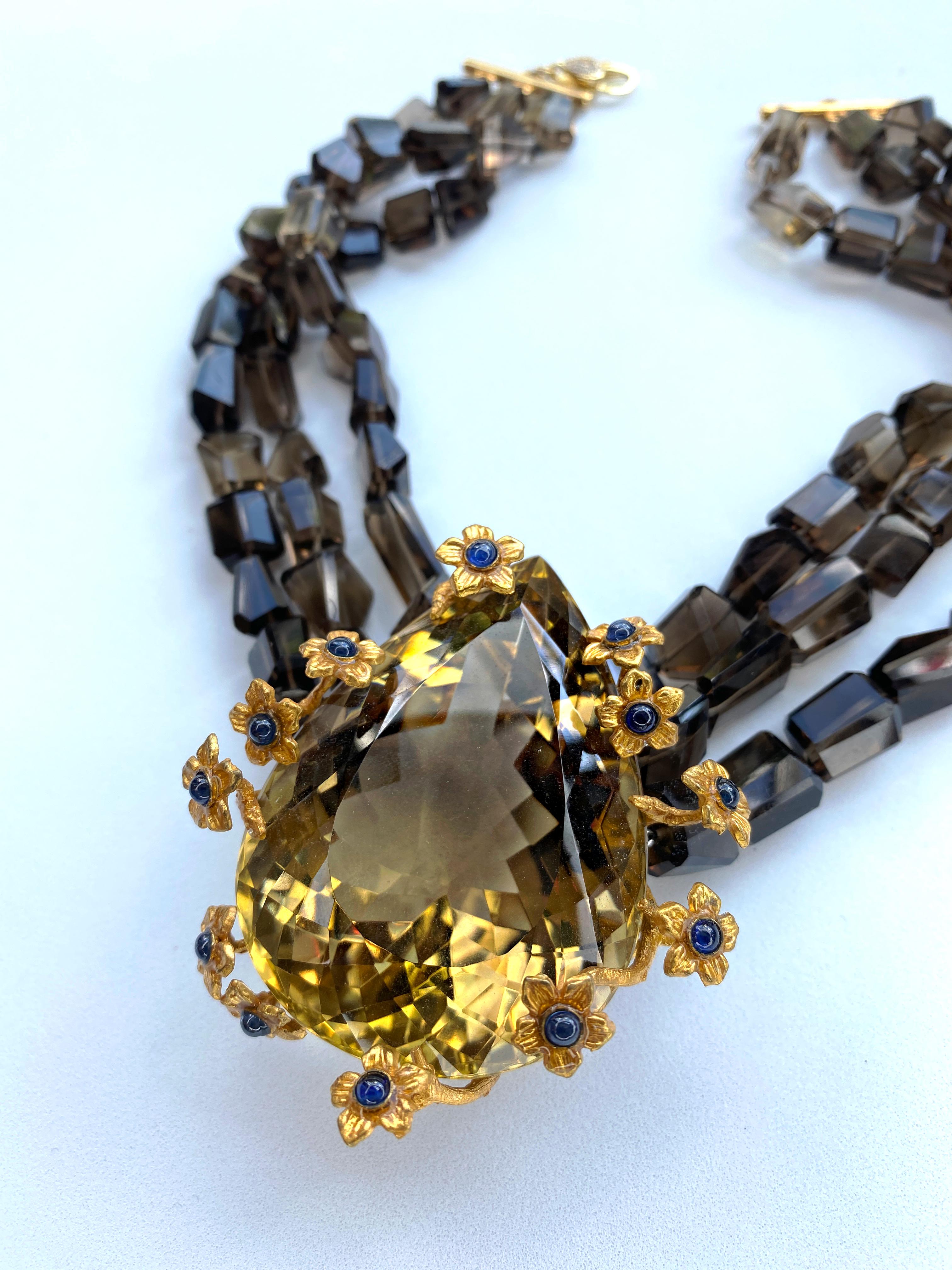 This glorious necklace features 3 strands of step cut Smoky Quartz beads and feature a Gold Filled vine wreath with blooming flowers, set with cabochon Sapphires delicately nesting an impressive natural 534 Ct Citrine from southern Spain. This