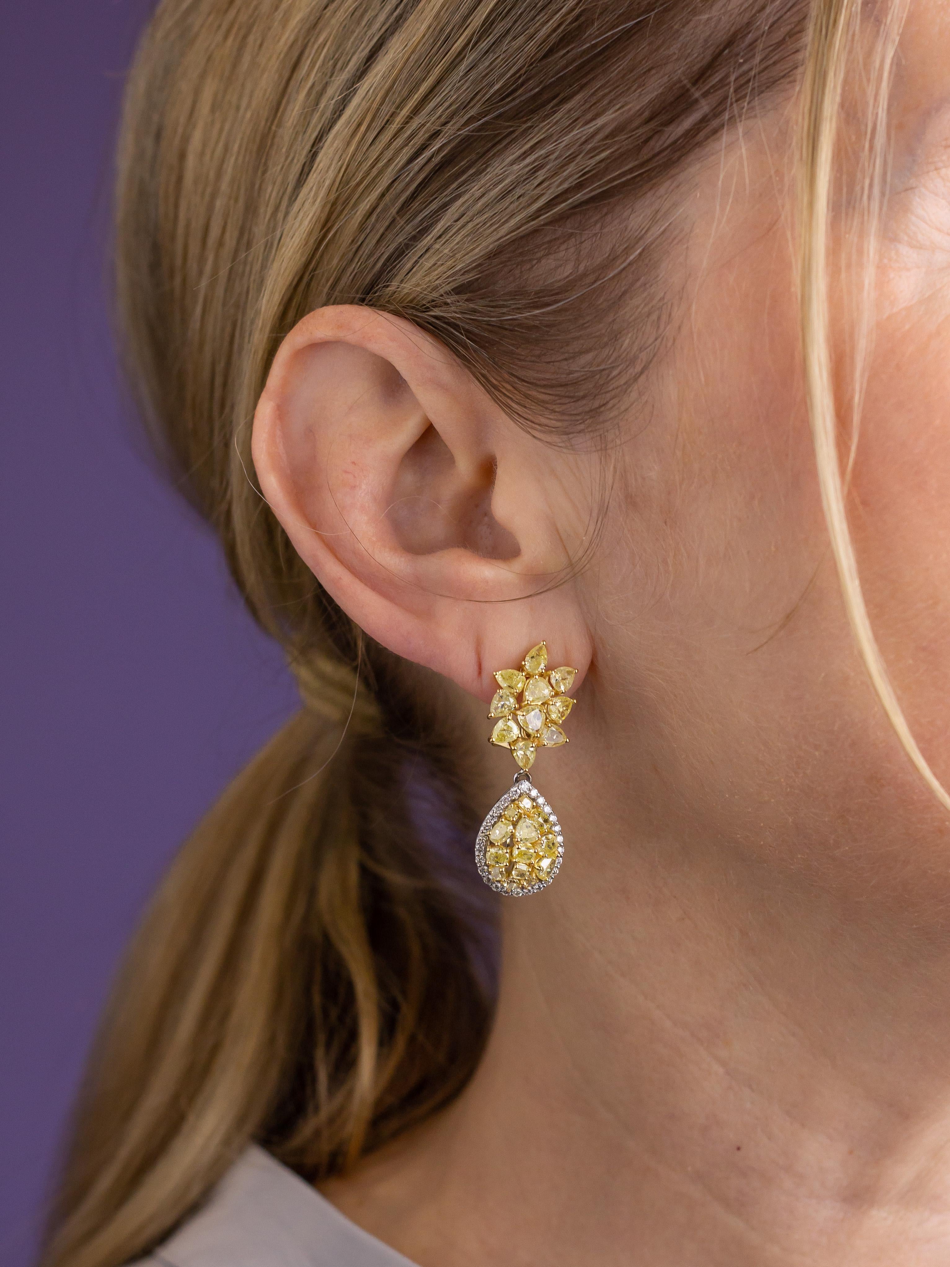 This pair of impressive drop earrings are crafted from 18 karat yellow gold and have been set with an array of yellow and white diamonds. The drop earrings stem from a cluster of three claw set pear shaped diamonds from which a teardrop pendant