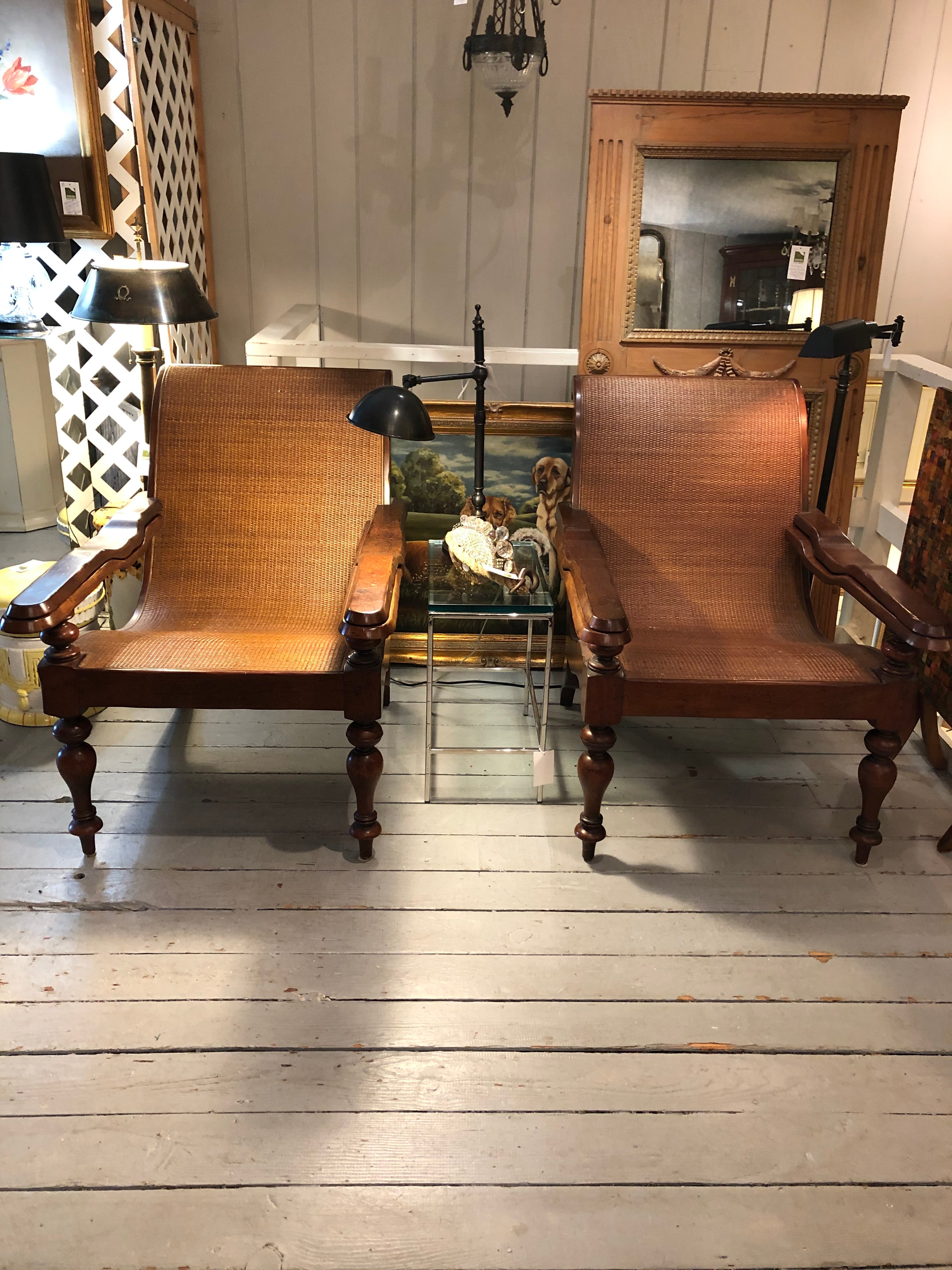 Handsome pair of teak & caned classic British style plantation chairs having sloped roomy silhouette and customary arms with leg extensions. Body of the chairs are tightly caned rattan. Seat height slopes from 14-18