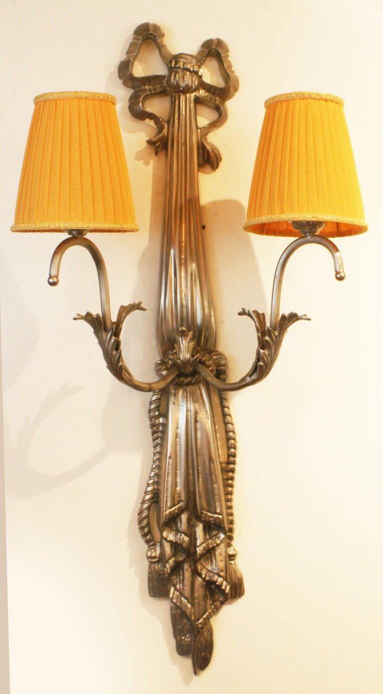 Pair of French Art Deco wall lights consists of a vertical nickel bronze structure having beautiful motif design with two curved arms of lights supporting two pleated “bistro” shape lampshades in light orange linen fabric. Lovely when the lights