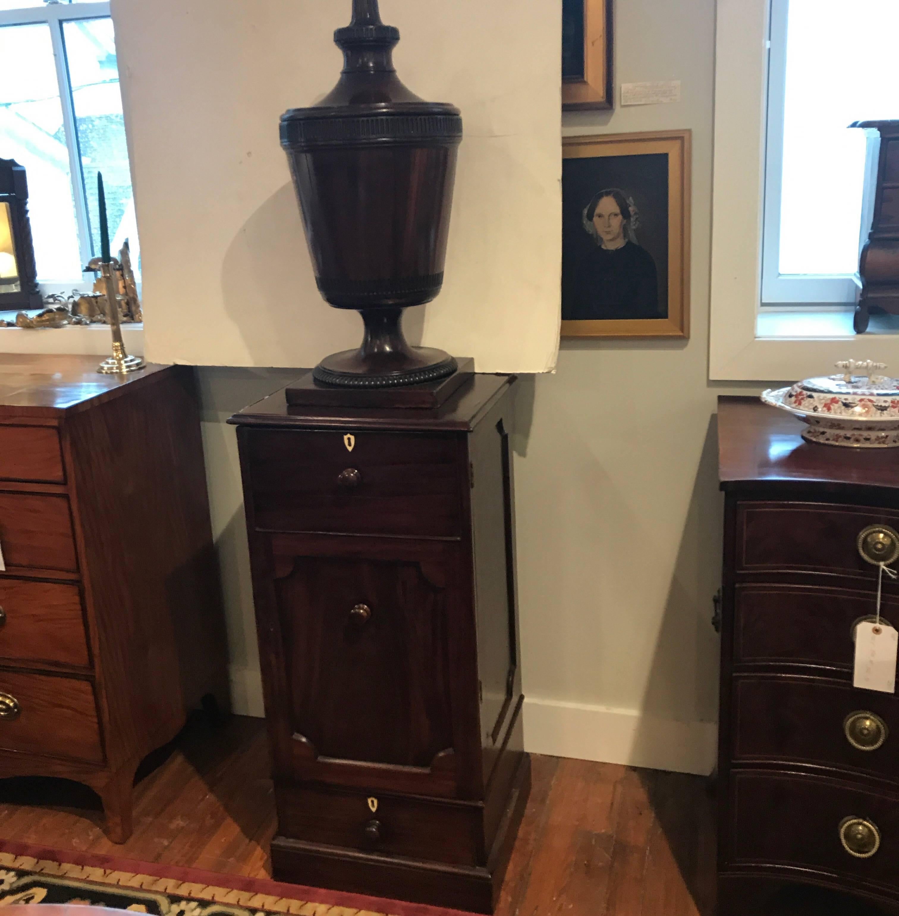 Large and impressive late 18th to early 19th century English mahogany urn on a cupboard stand. In two parts with leaf and chip carved urn resting on a molded base with panelled sides. The base with door opening to reveal shelves above a drawer,