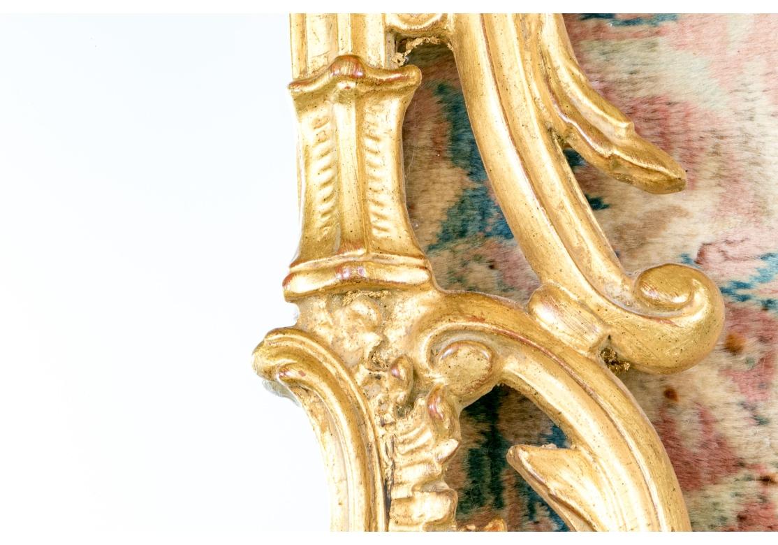 Impressionnant miroir rectangulaire arrondi de style rococo  dans un beau cadre doré  Le fronton est orné d'une fleur feuillue. Le périmètre intérieur du cadre présente des motifs en forme de colonnes avec des volutes élégamment incurvées aux
