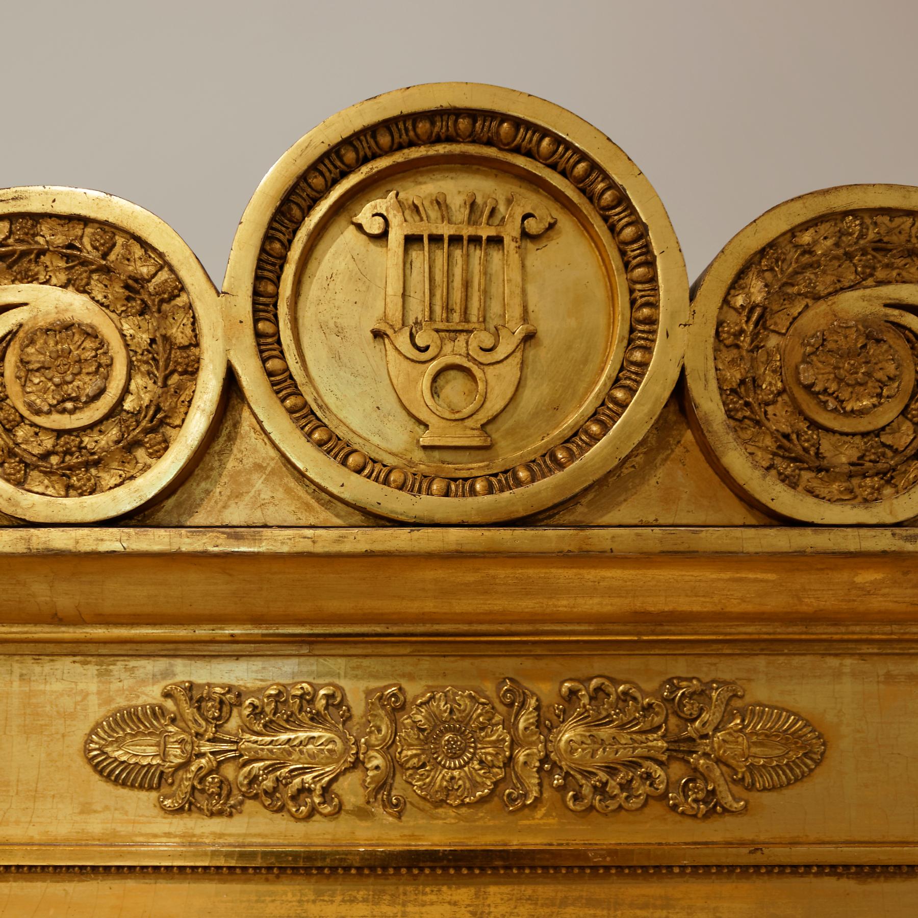 Un rare miroir trumeau Empire allemand du début du 19e siècle en bois doré. La grande plaque rectangulaire est surmontée d'un fronton à volutes enrichi de feuilles de vigne et d'un médaillon central renfermant une lyre classique. Les côtés du miroir