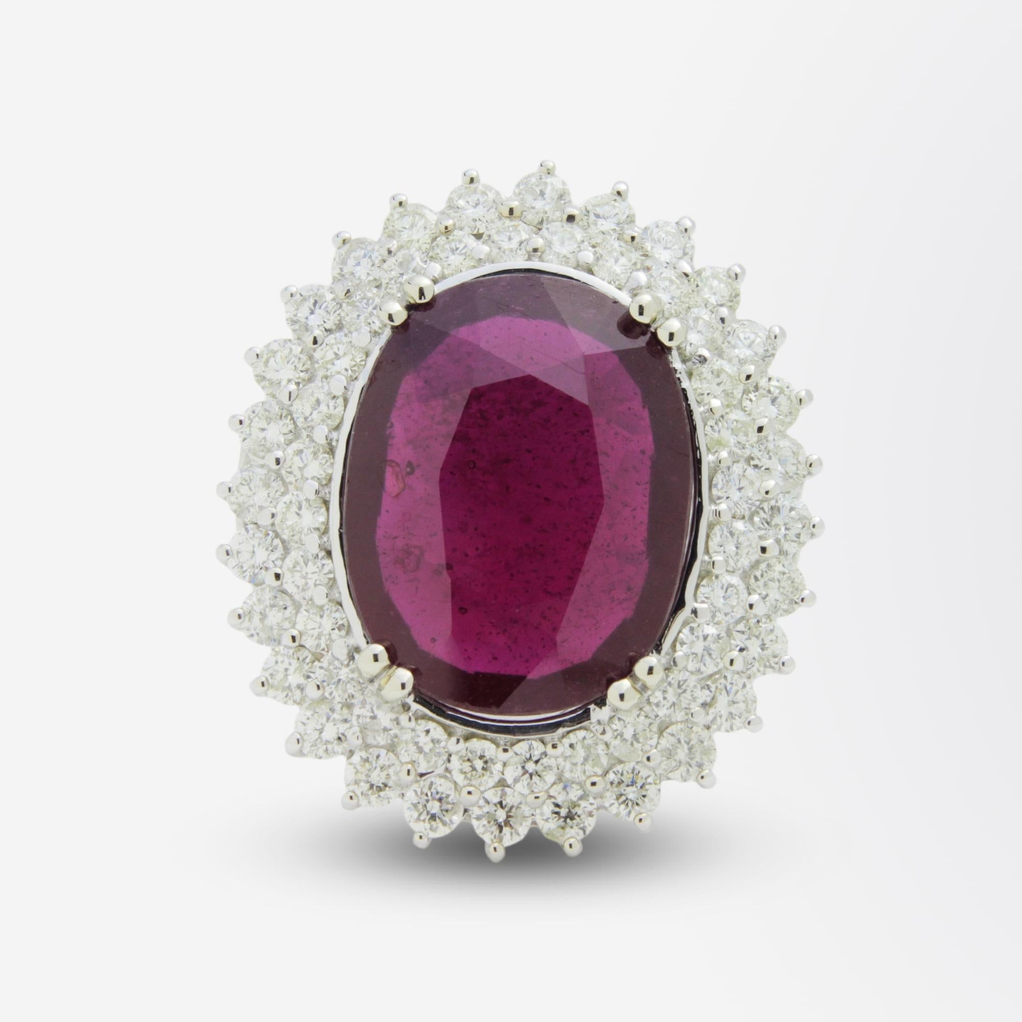 A very bold white gold ring containing a large, oval cut, fracture filled (glass) ruby surrounded by brilliant cut diamonds. The ring is crafted from 14 karat white gold and contains the central ruby estimated at 12 carat, which has two halos of