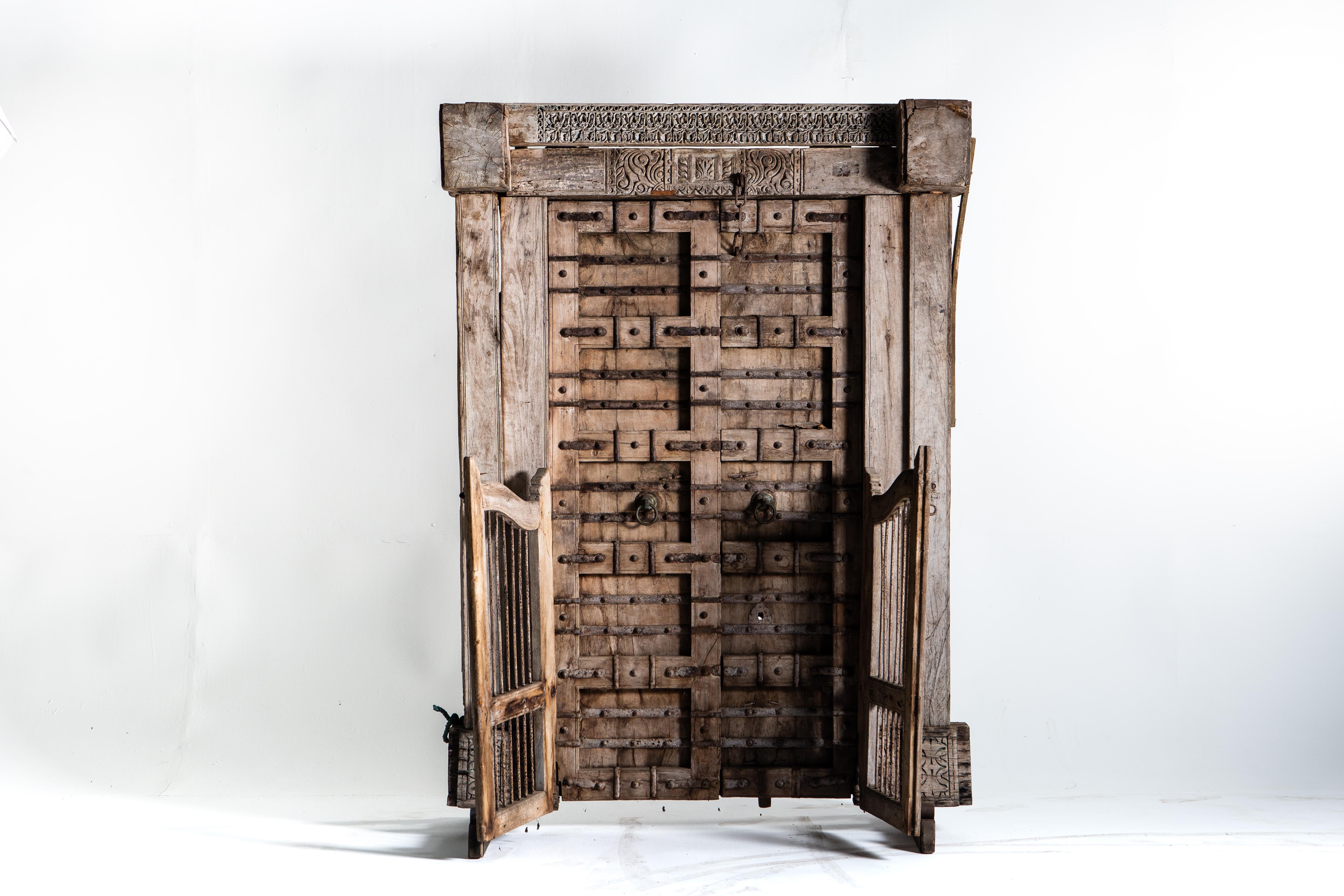 This complete entryway is as handsome as it is imposing. Delicate carvings are featured at the top and bottom of the frame. The two main doors are highly reinforced with heavy beans and hand forged iron straps. The open inward and are secured with a