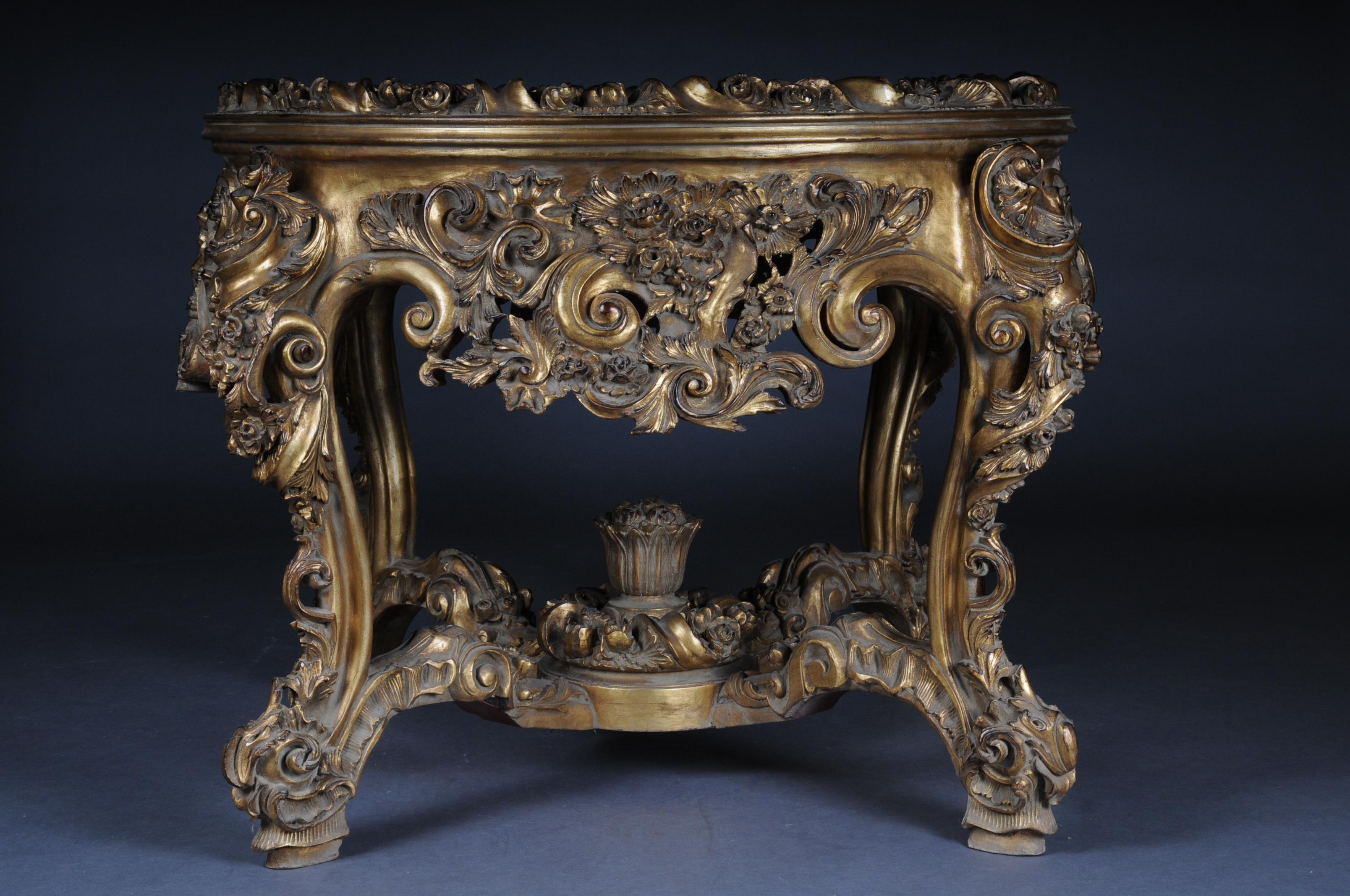 High quality solid beechwood finely carved down to the last detail. Gold taken. On curved, carved legs, connected with X-shaped, heavily carved gutter. Ornamented frame with garlands. Overhanging, profiled, round tabletop. On the cover plate, a