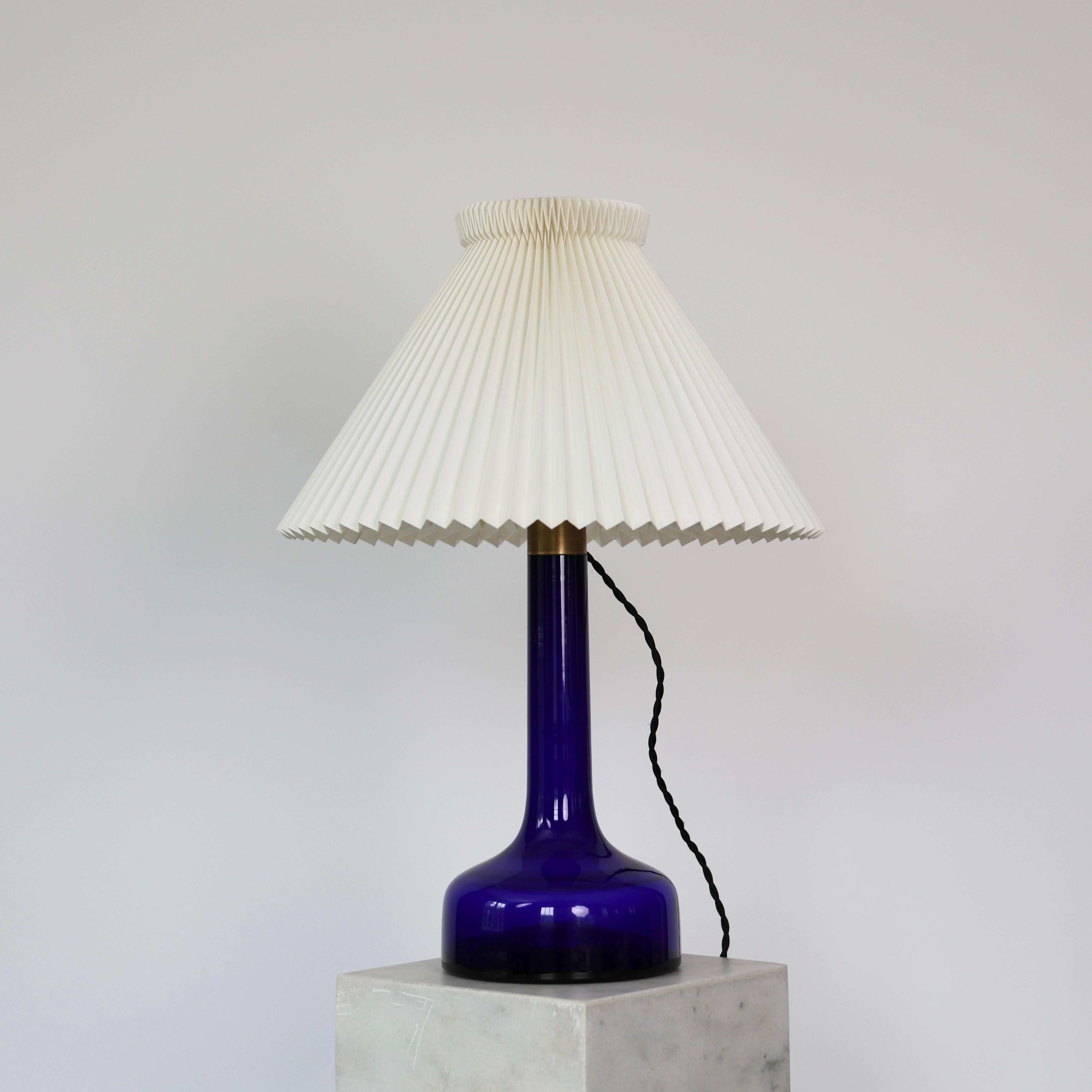 Impressive Blue Glass Table Lamp made by Le Klint in the 1950s.

* Large blue glass table lamp with a white hand-pleaded shade
* Designer: Gunnar Biilmann Petersen
* Model: 302
* Producer: Le Klint
* Producer (Glass base): Kastrup Glasverk now