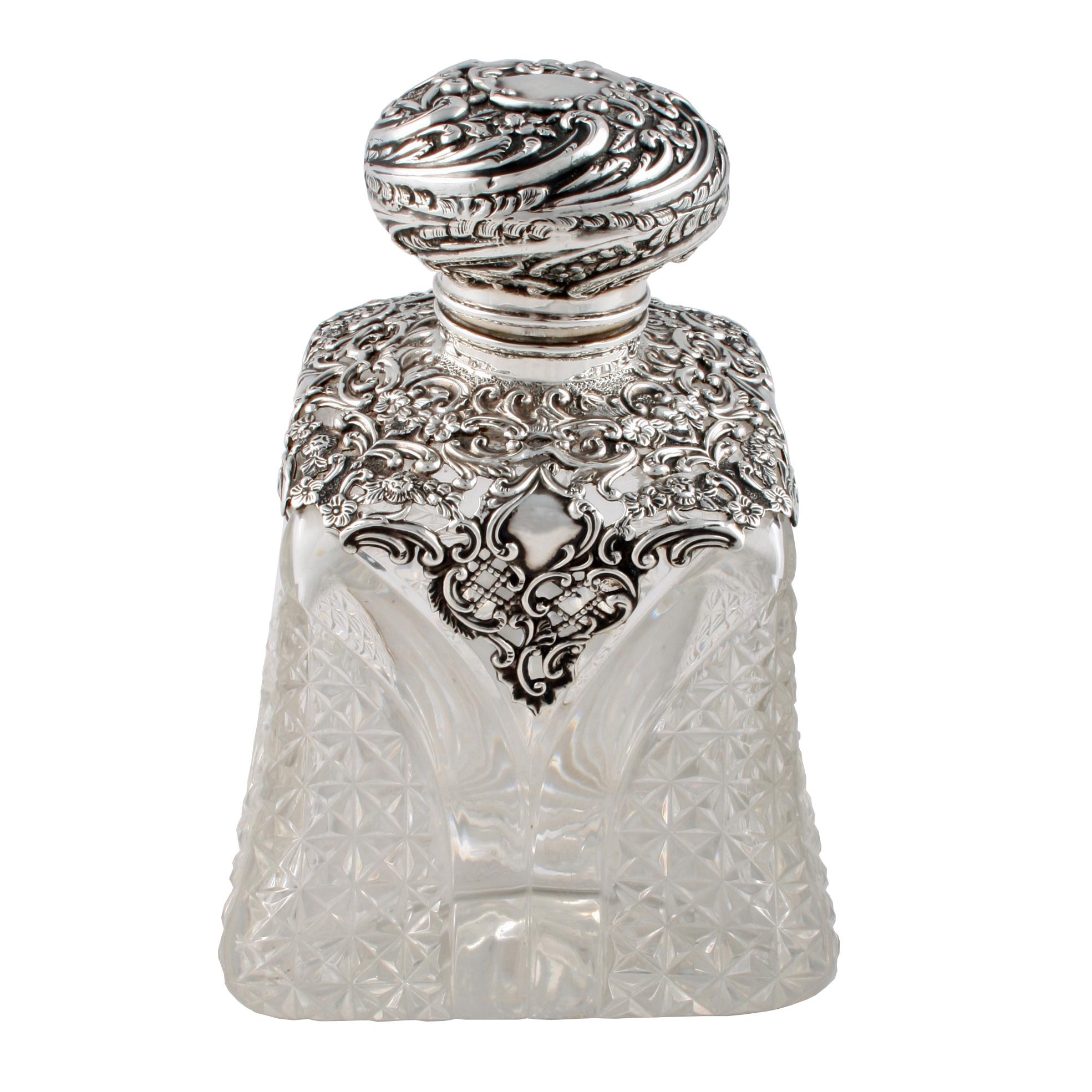 A large late Victorian cut crystal perfume bottle.

The perfume bottle has a sterling silver hall marked collar and hinged lid.

The bottle has a square base with concave heavily cut sides and a square cut underside.

The sterling silver
