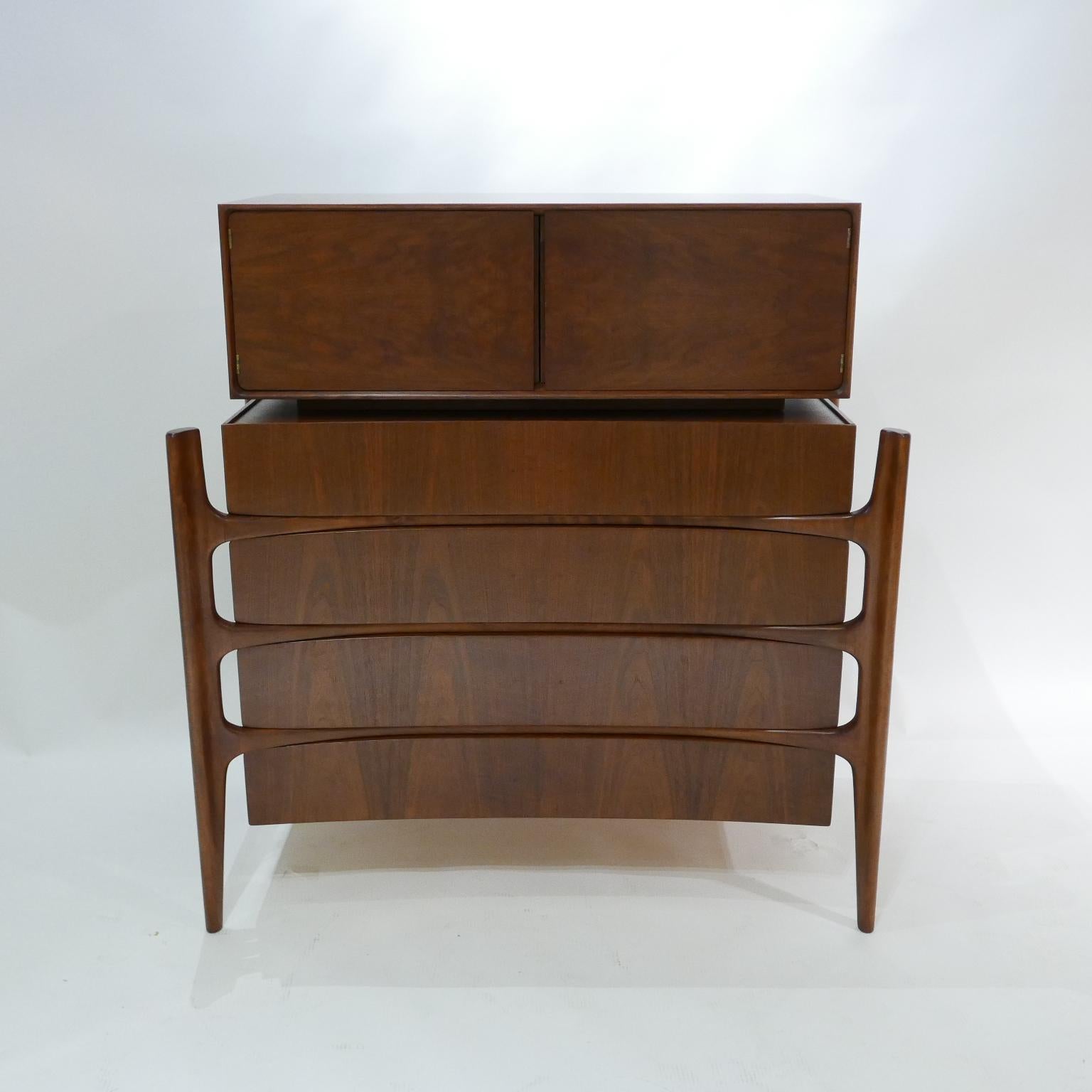 Exposed carved walnut legs with a curved bookmatched walnut front. Beautiful and Sculptural four drawer chest with 2 door top cabinet designed by William Hinn for Urban Furniture's 