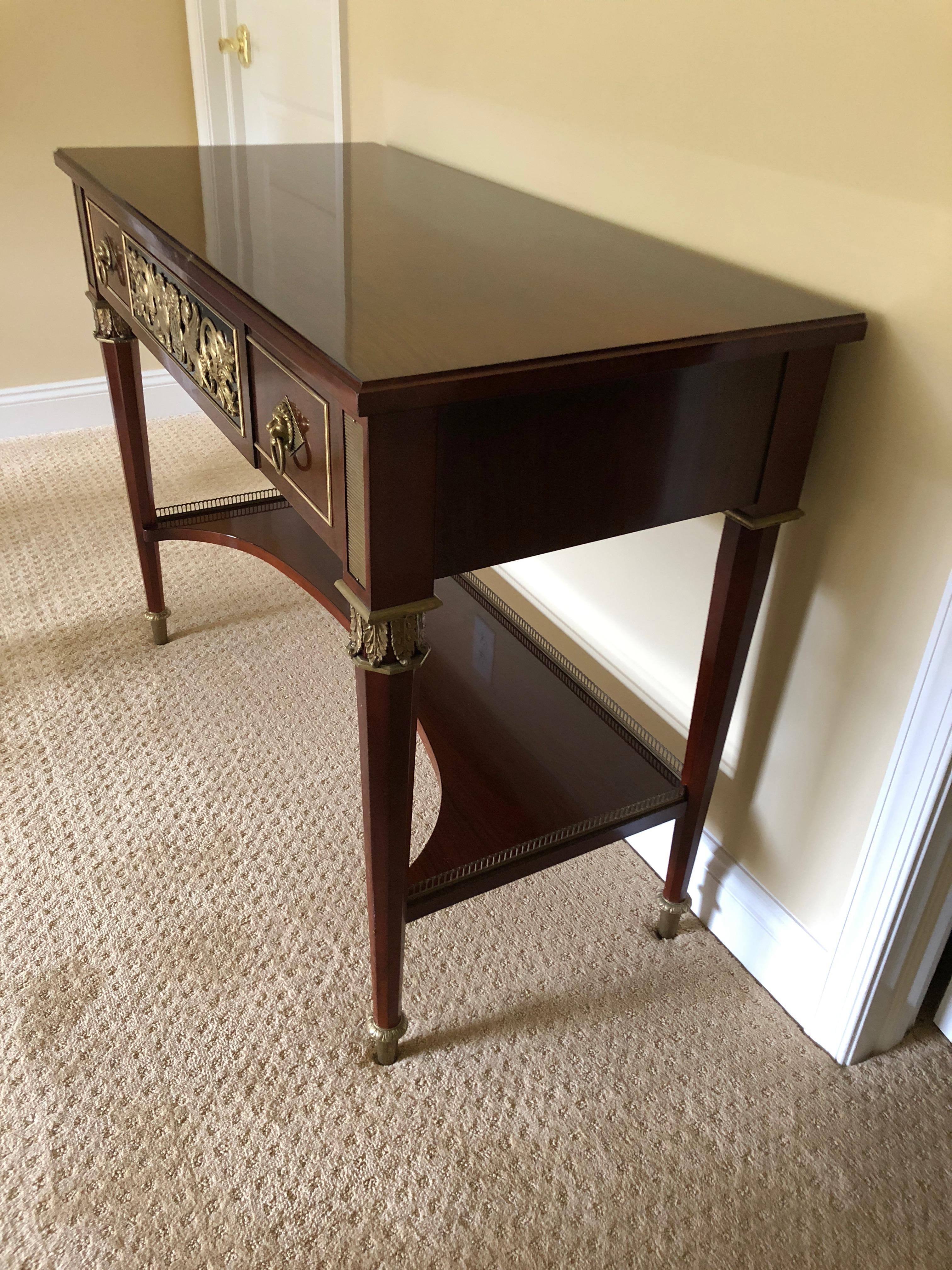 A very rich mahogany neoclassical style console table beautifully crafted by John Widdicomb, having ebonized front centre drawer with gorgeous brass decoration flanked by two smaller drawers with handsome lion head hardware. A second lower tier has
