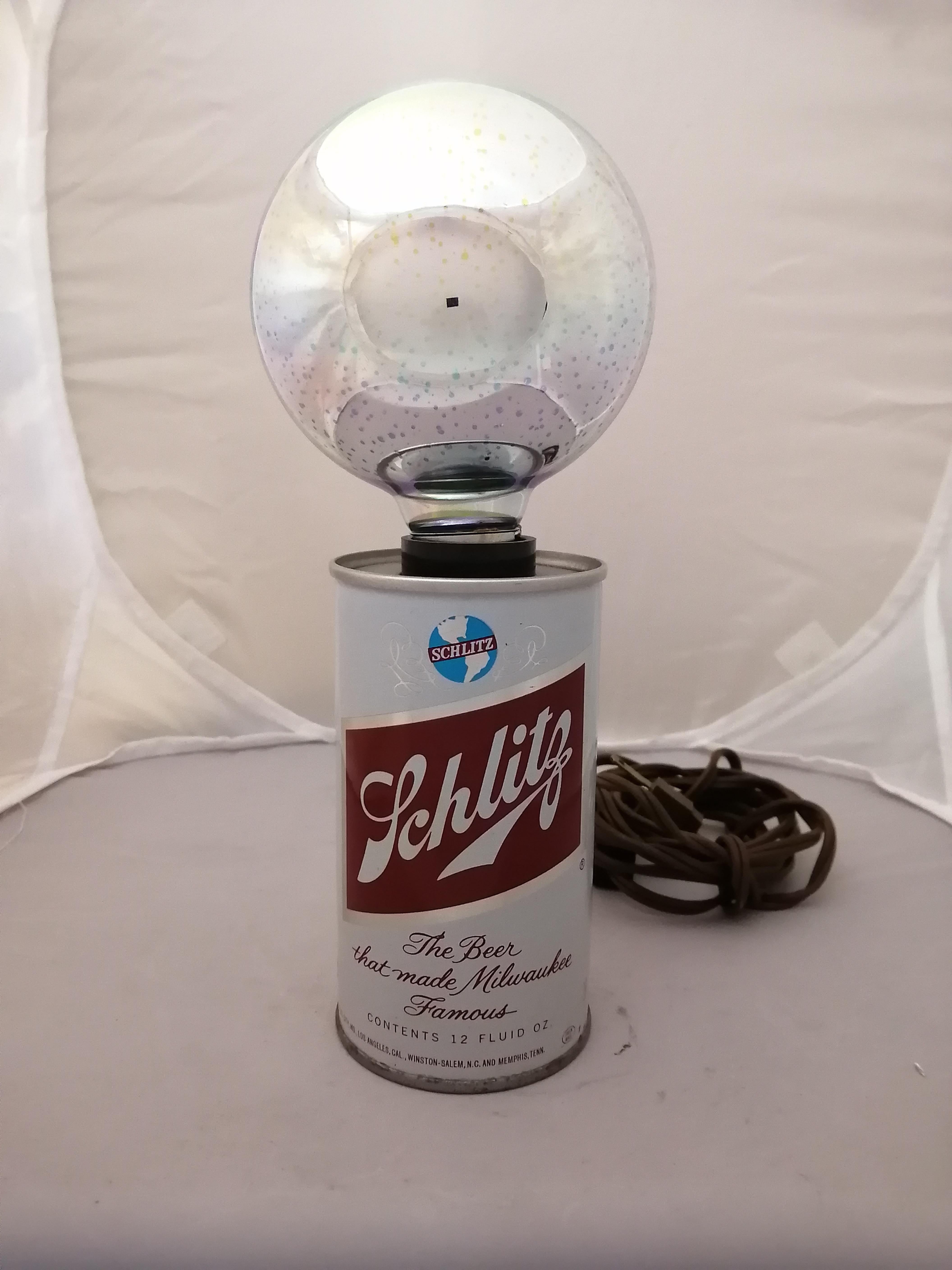 Lampe de table américaine des années 1970 en forme de canette de bière Schlitz par la société IMS. La lampe comprend une ampoule multicolore pour remplacer l'ampoule originale manquante. Présence d'un autocollant sur le dessus. Boîte d'origine