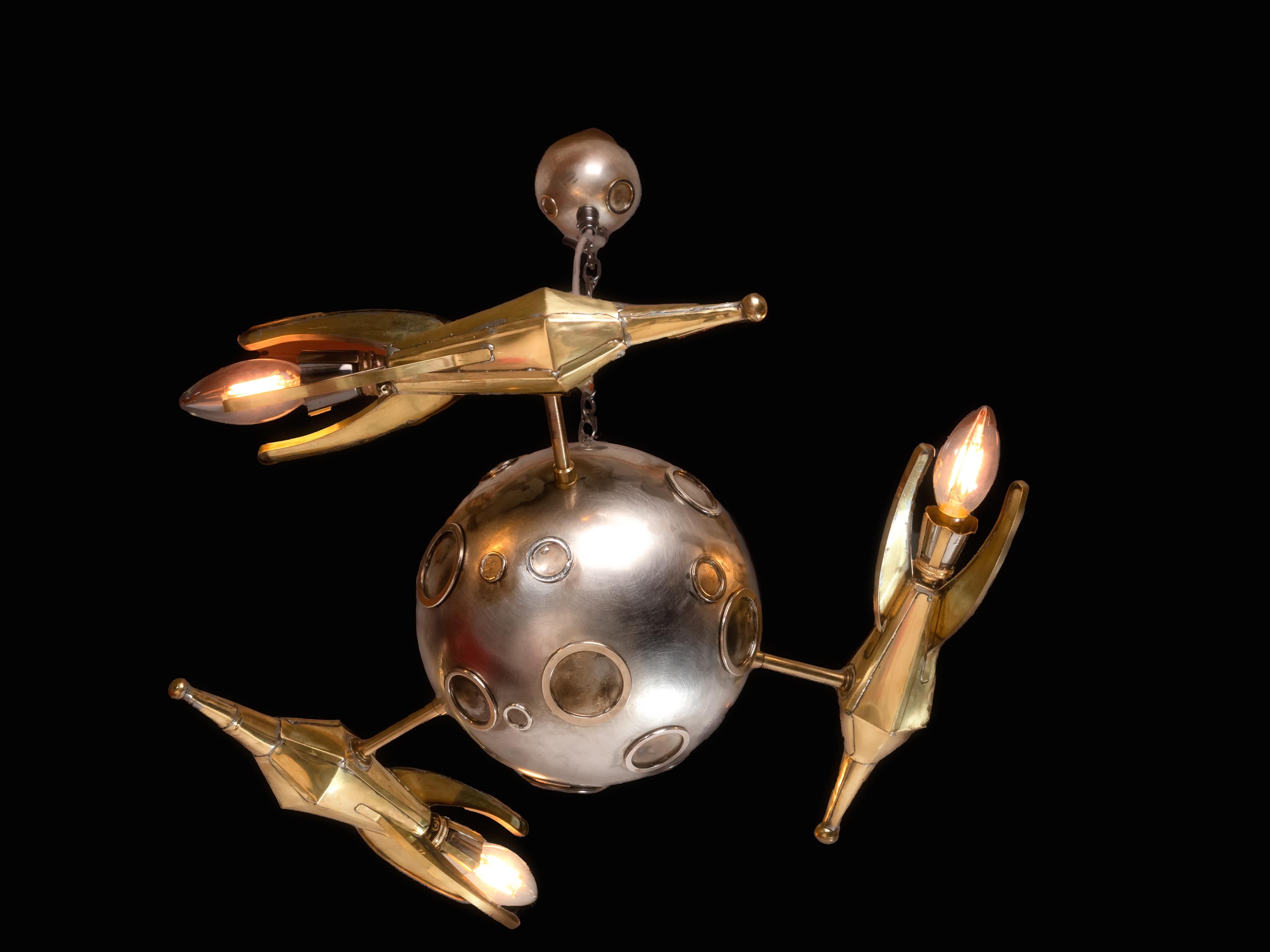 In Orbit, is a playful look at ceiling lights, leaning heavily on a early 20th century expectation of space travel. This ceiling light ever entertains with three rockets orbiting the moon (respect is due here to Antoine de Saint-Exupery) whilst