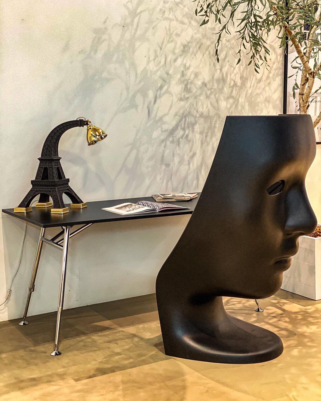 A life-size Greek mask becomes an inhabitable throne. The Nemo Swivel Armchair is carved from a single block of matte-black polyethylene, its classical profile turned outward while the hollowed interior cradles the sitter. Mounted on a hidden 360°