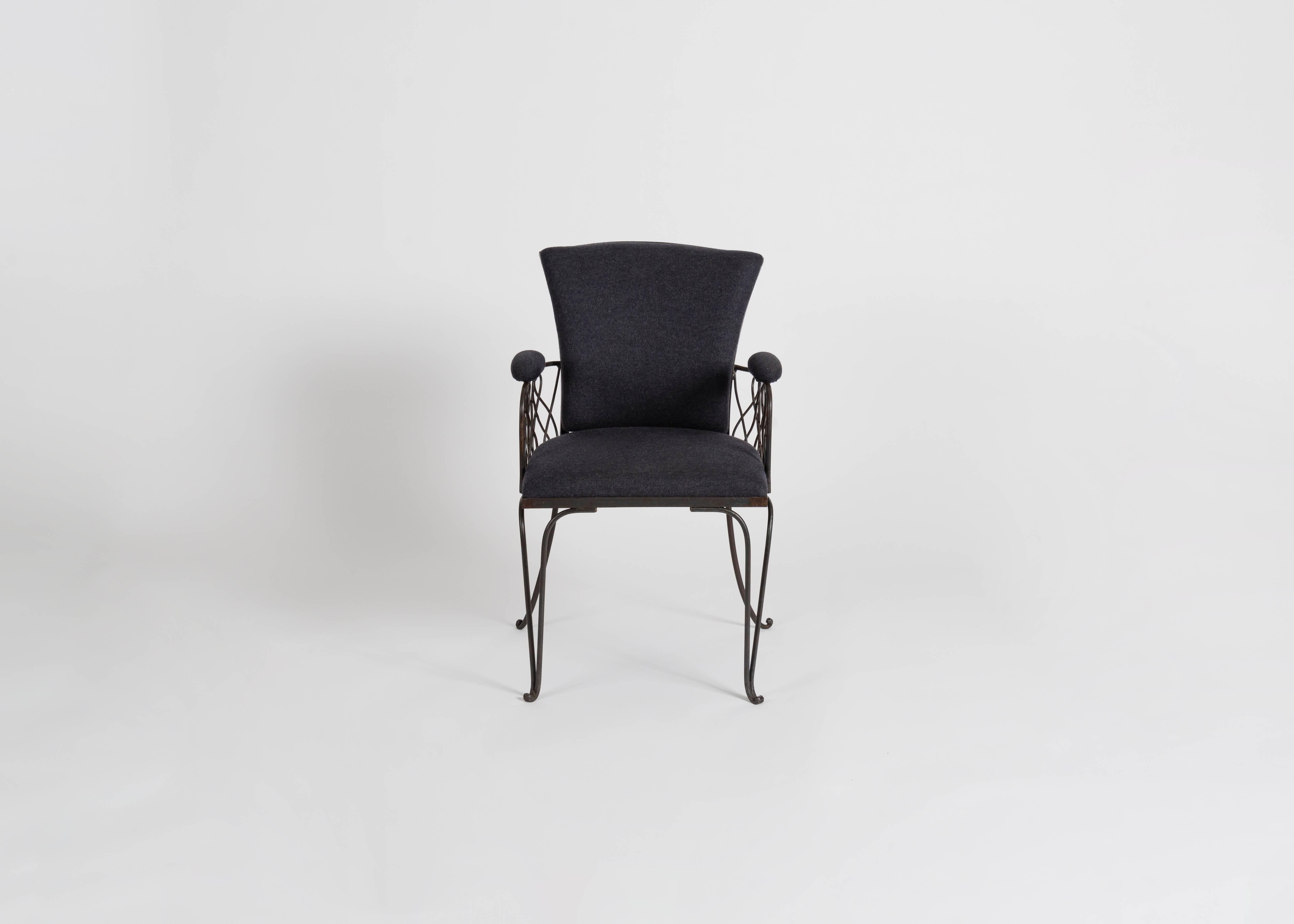 A wrought iron chair in the manner of Jean Pascaud, featuring elegantly splayed feet, a broad back, and crisscrossing supports under each arm.