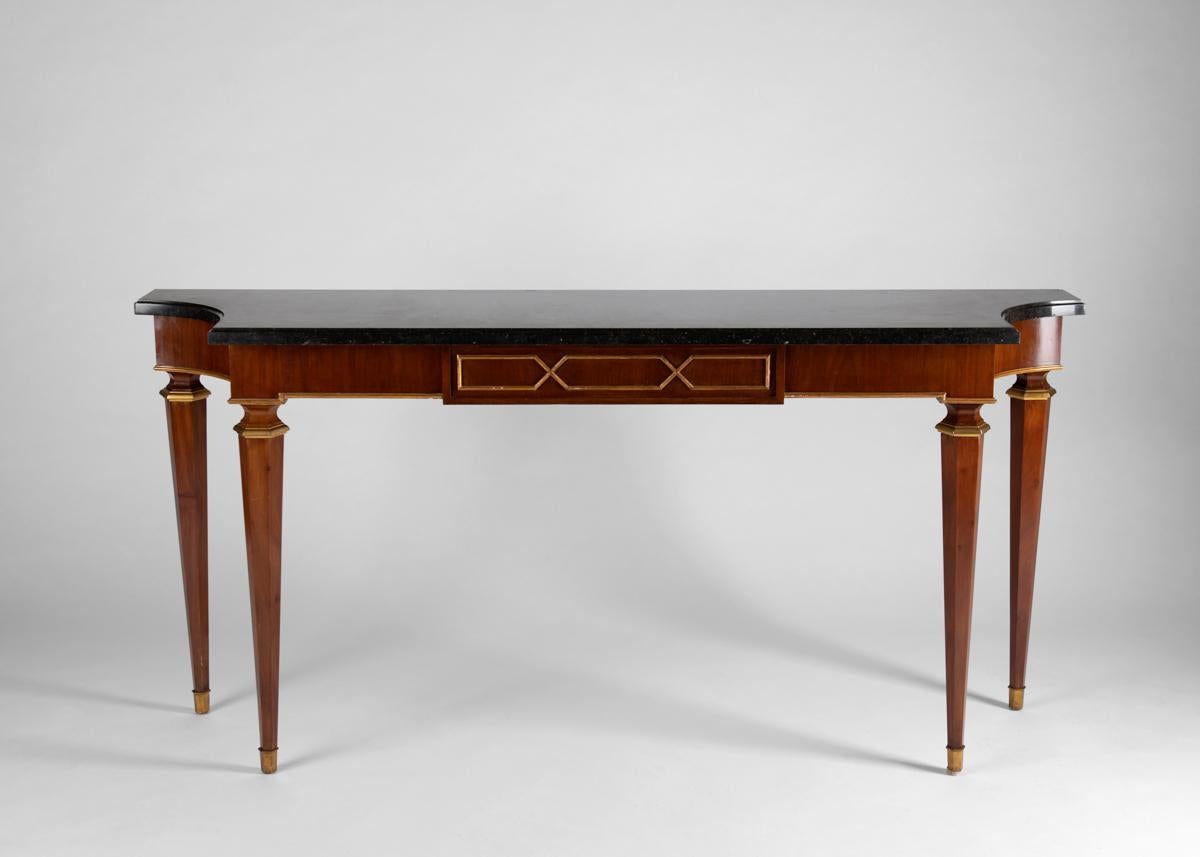 A stately, large-scale console featuring a lovely black marble poised upon hexagonal tapered legs with gilt wood accents. Its feet and details in bronze. In the manner of Lucien Rollin.