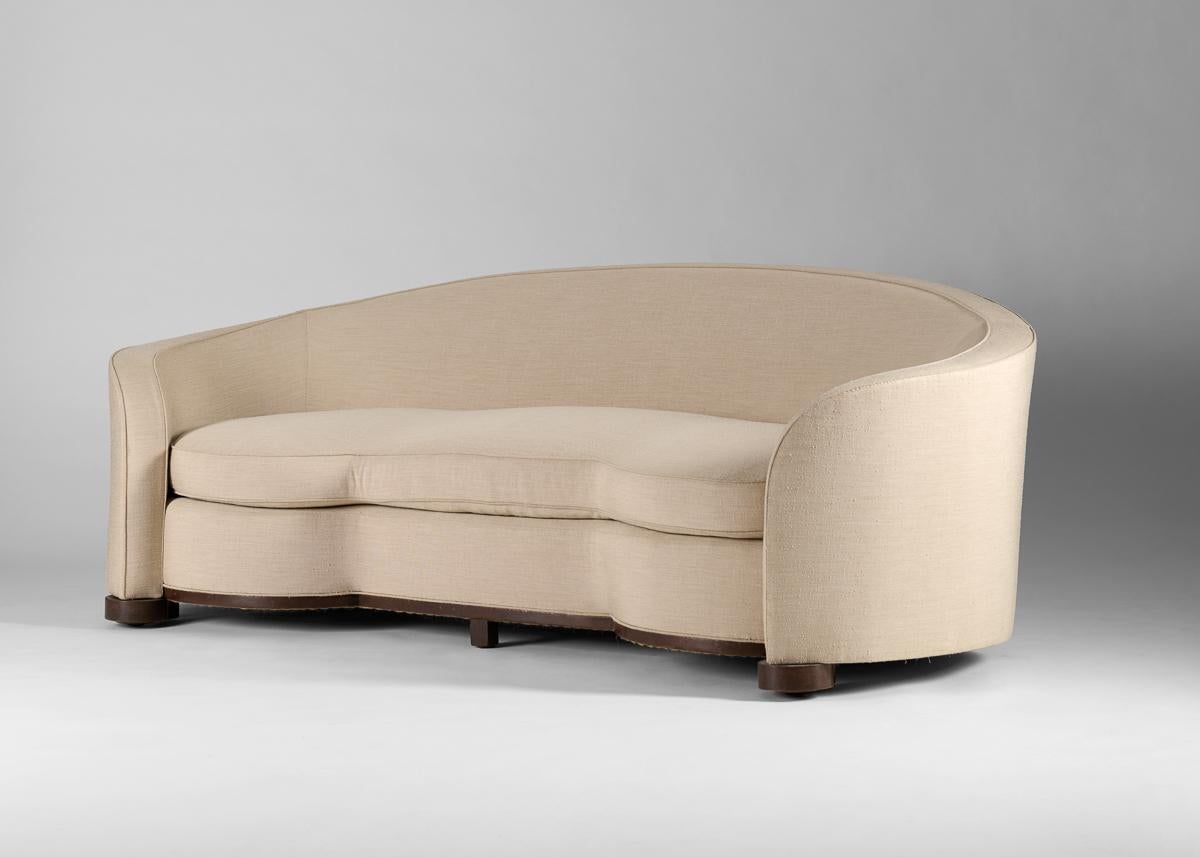 With its soaring back, rounded seats on either end, and arms that curve around the frame, this grand, luxurious sofa is characteristic of Jules Leleu's work from the 1930s — possessed of a certain reserved flare, and executed with the utmost