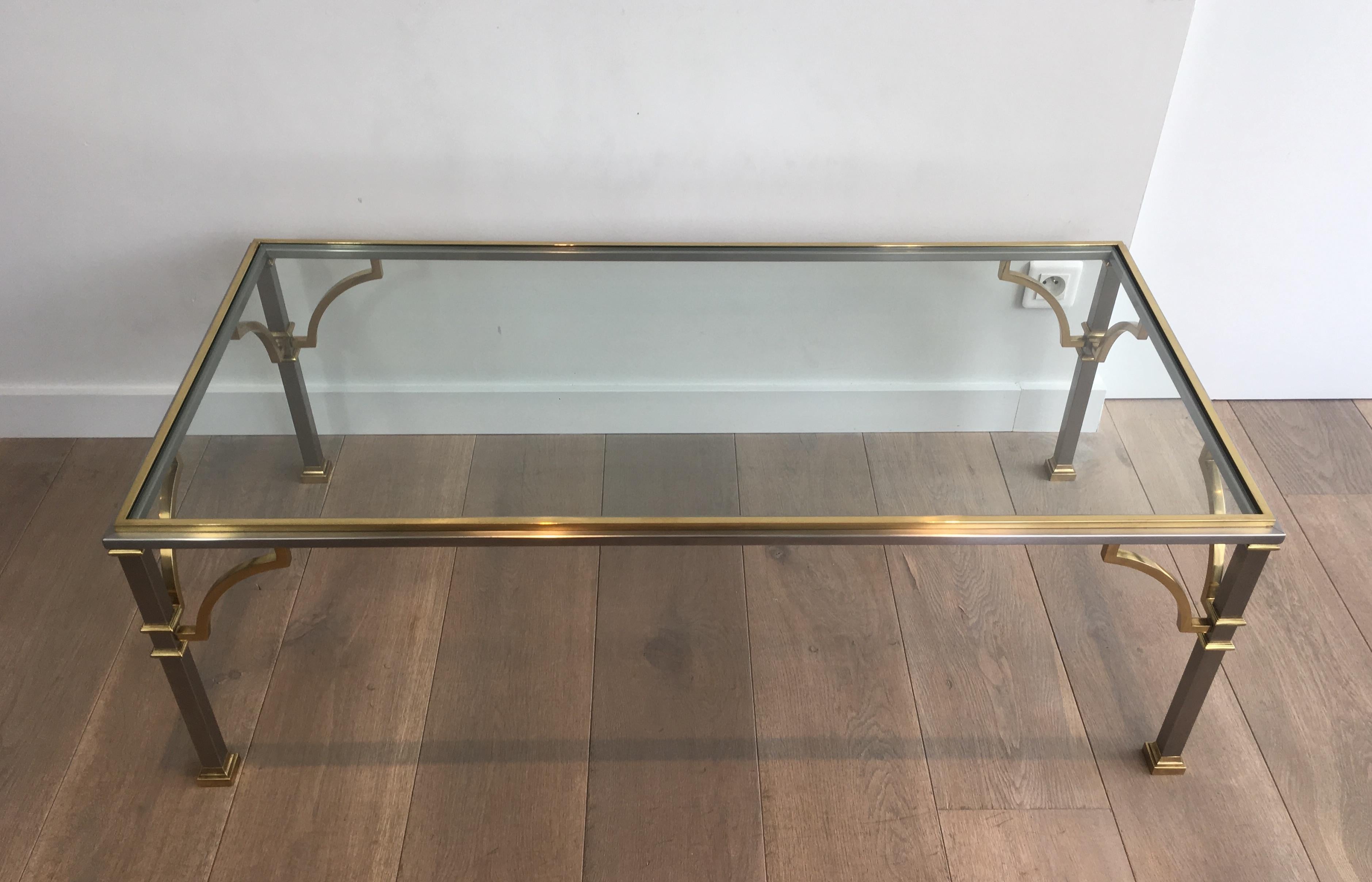 This neoclassical coffee table is made of brushed steel and brass with a glass shelf. This is a French work in the style of famous Maison Jansen designer, circa 1970.