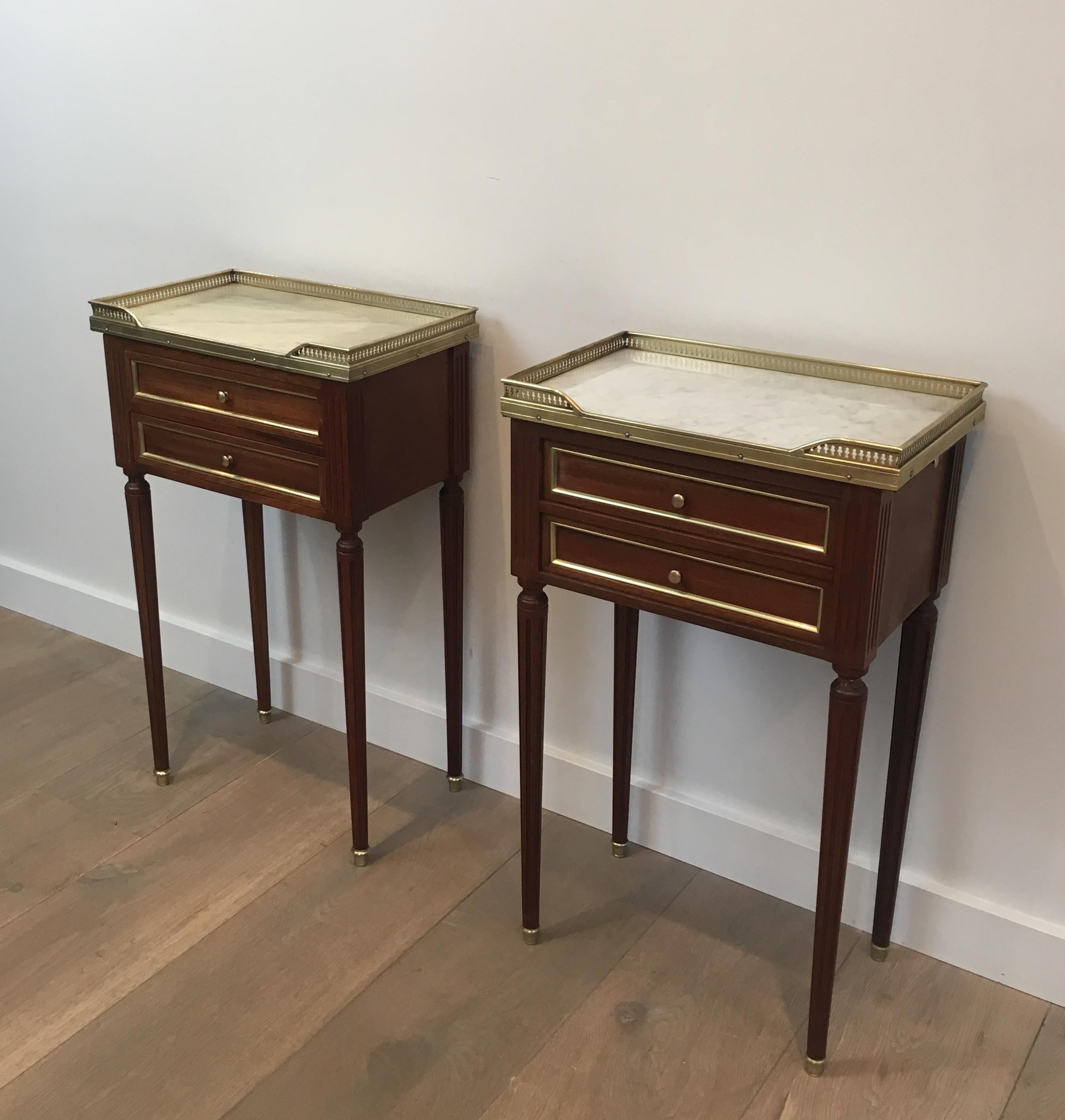 This pair of neoclassical style side tables is made of mahogany and brass with white marble tops. On the side of each end table, there is a sliding shelve with a leather on top. The color of the marble is a slightly different on each side table but
