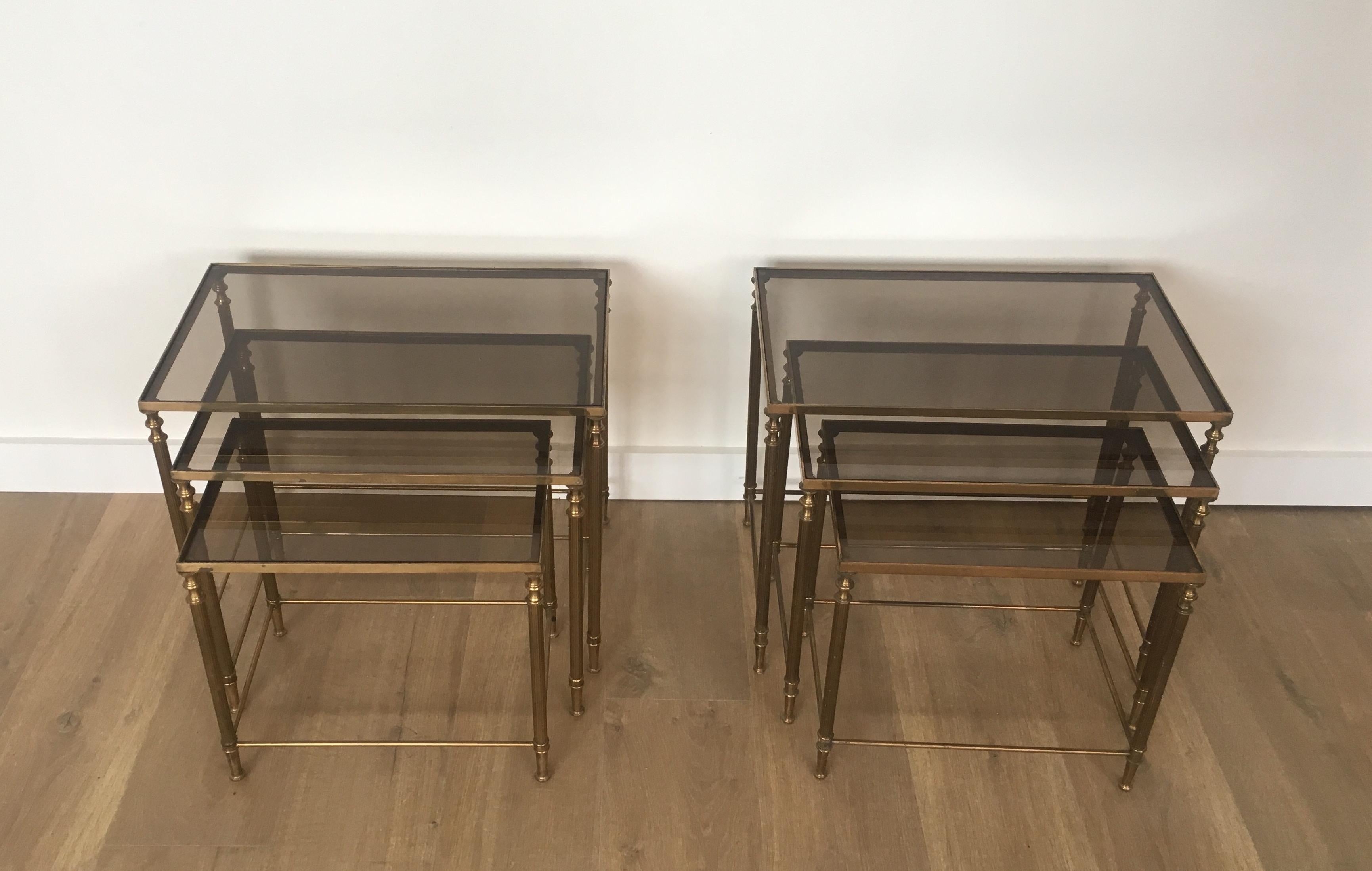 This pair of neoclassical style brass nesting tables are made of brass with smoked glass tops. This model is in the style of famous French designer Maison Jansen, circa 1940.
