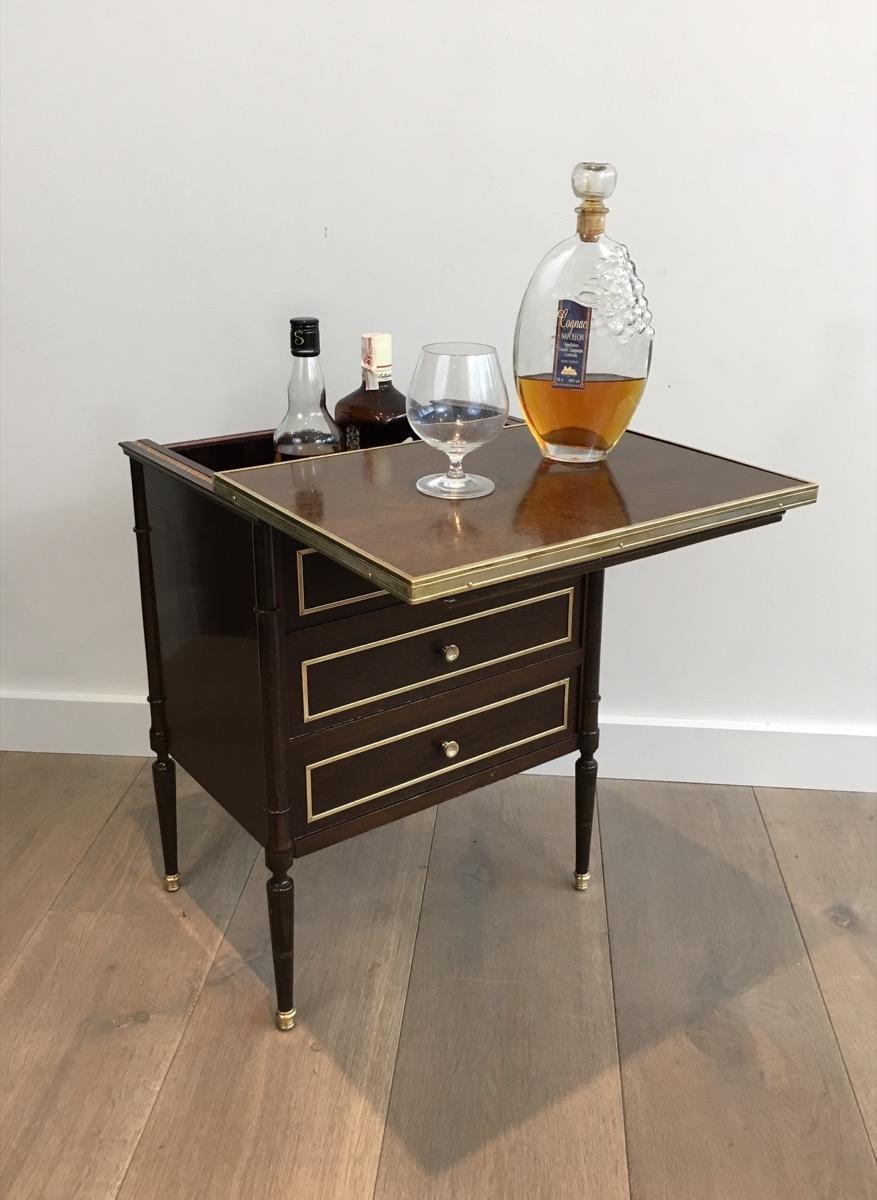 This unusual and rare neoclassical small drawer table made of mahogany and brass is in fact a bar. The drawers cannot be open and the top is sliding to let discover a small bar on which bottles and glasses can be stored. This is a French work, in