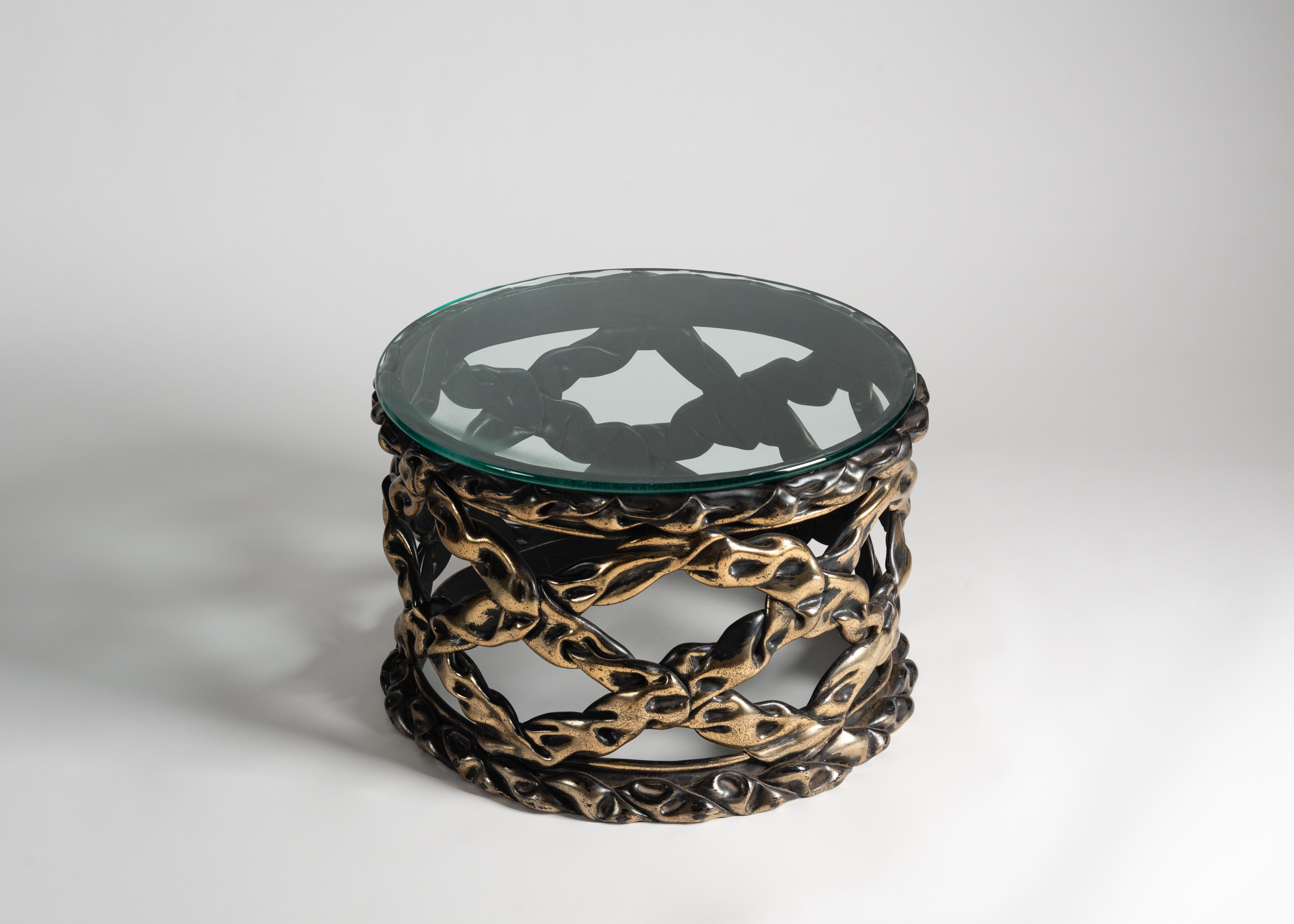 With a top of glass and a base of bronze-colored resin modeled into a cylinder of latticed ribbons, this table, in the style of Tony Duquette, possesses a unique dark beauty.

