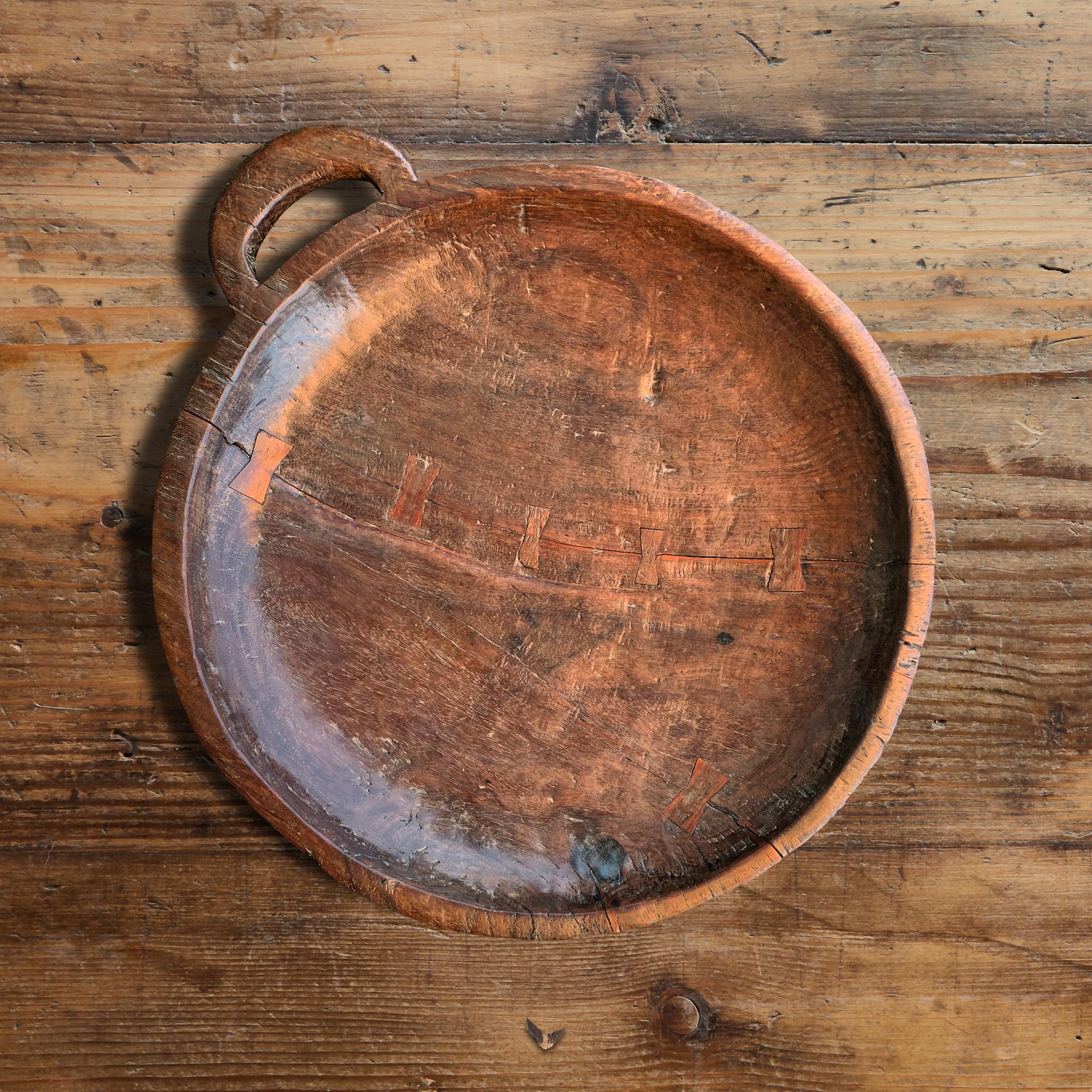 An incredible 18th century, or earlier, English mahogany platter hand carved of one piece of wood, with a handle on one side, butterfly joint repairs, and a fantastic patina that only hundreds of years of use could bestow.