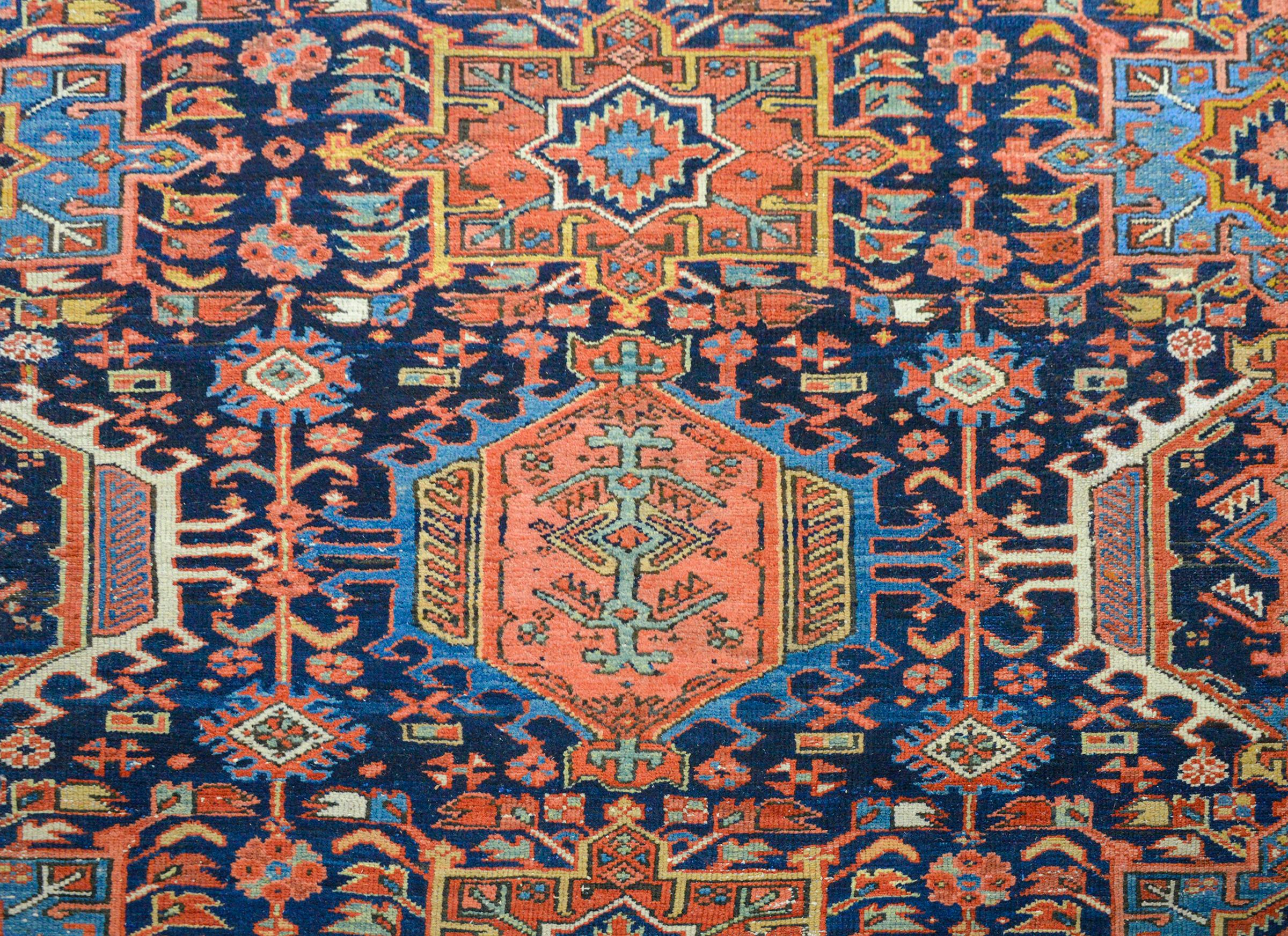 An incredible early 20th century Persian Karaje Serapi rug with a field of all-over large-scale stylized flowers amidst a field of more flowers and vines on a dark indigo background. The border is exceptional, with a repeated large-scale floral