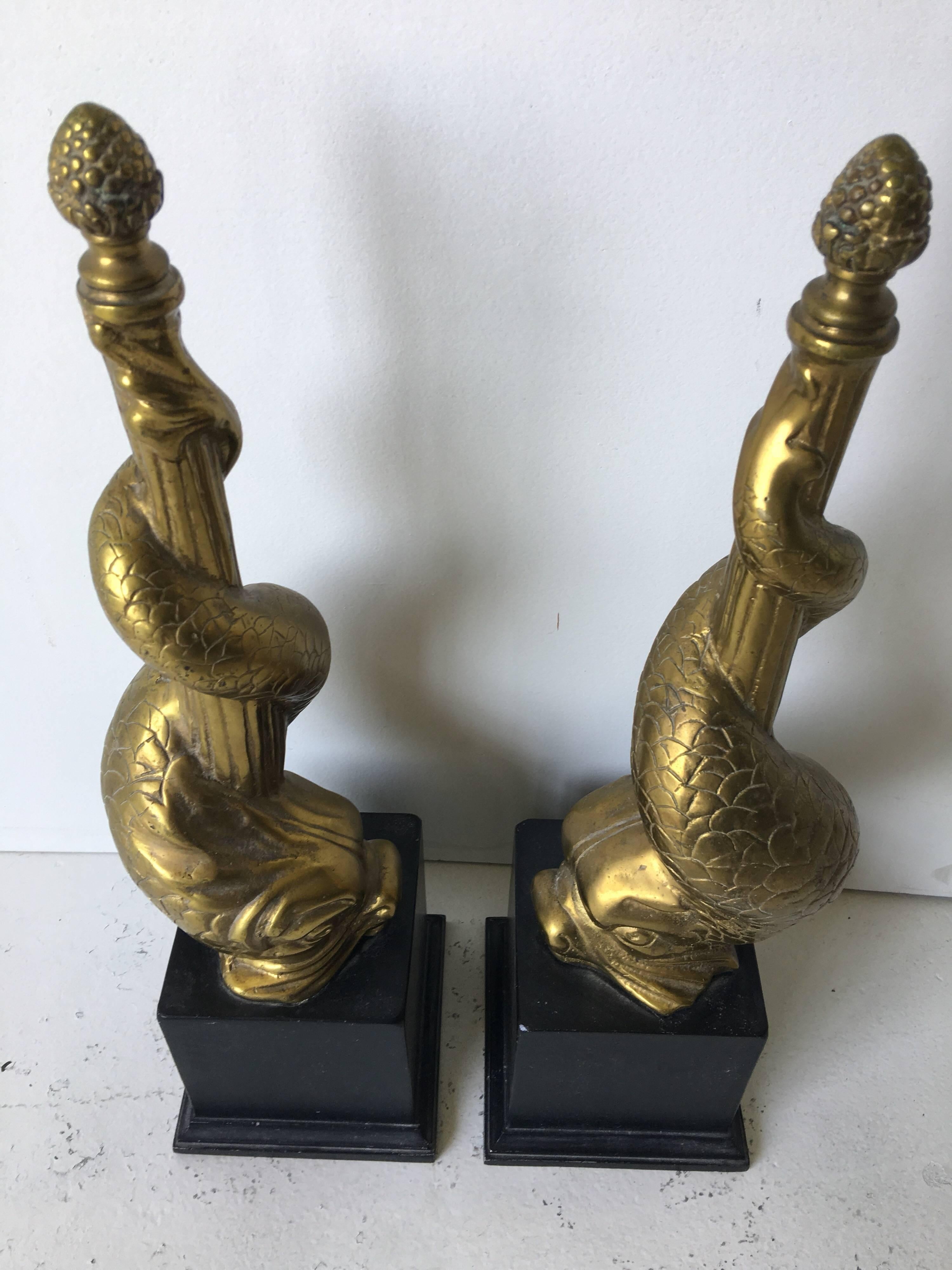 These are absolutely wonderful! These fireplace ornaments rest out in front, and feature downward spiraling figural dolphins on pedestals. There are finials to tops of fluted rods. Great Chenets or Andirons. They are very heavy in brass with cast