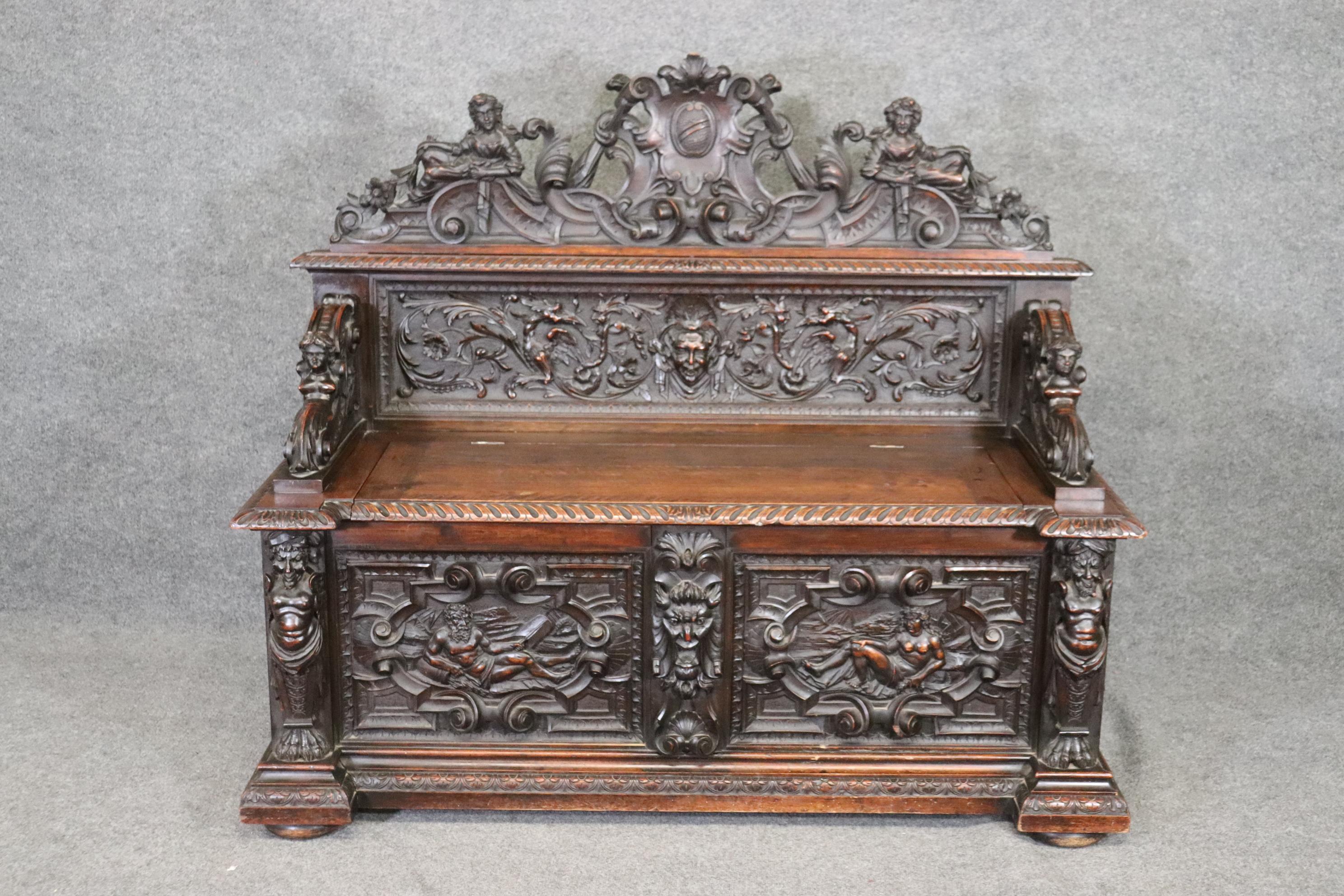 This is an incredibly and profusely carved Italian Luigi Frullini or RJ Horner Style hall bench with every possible carved cherub, satyr and mythical creature. The piece is in good condition with no major issues and has a trunk for hiding away shoes