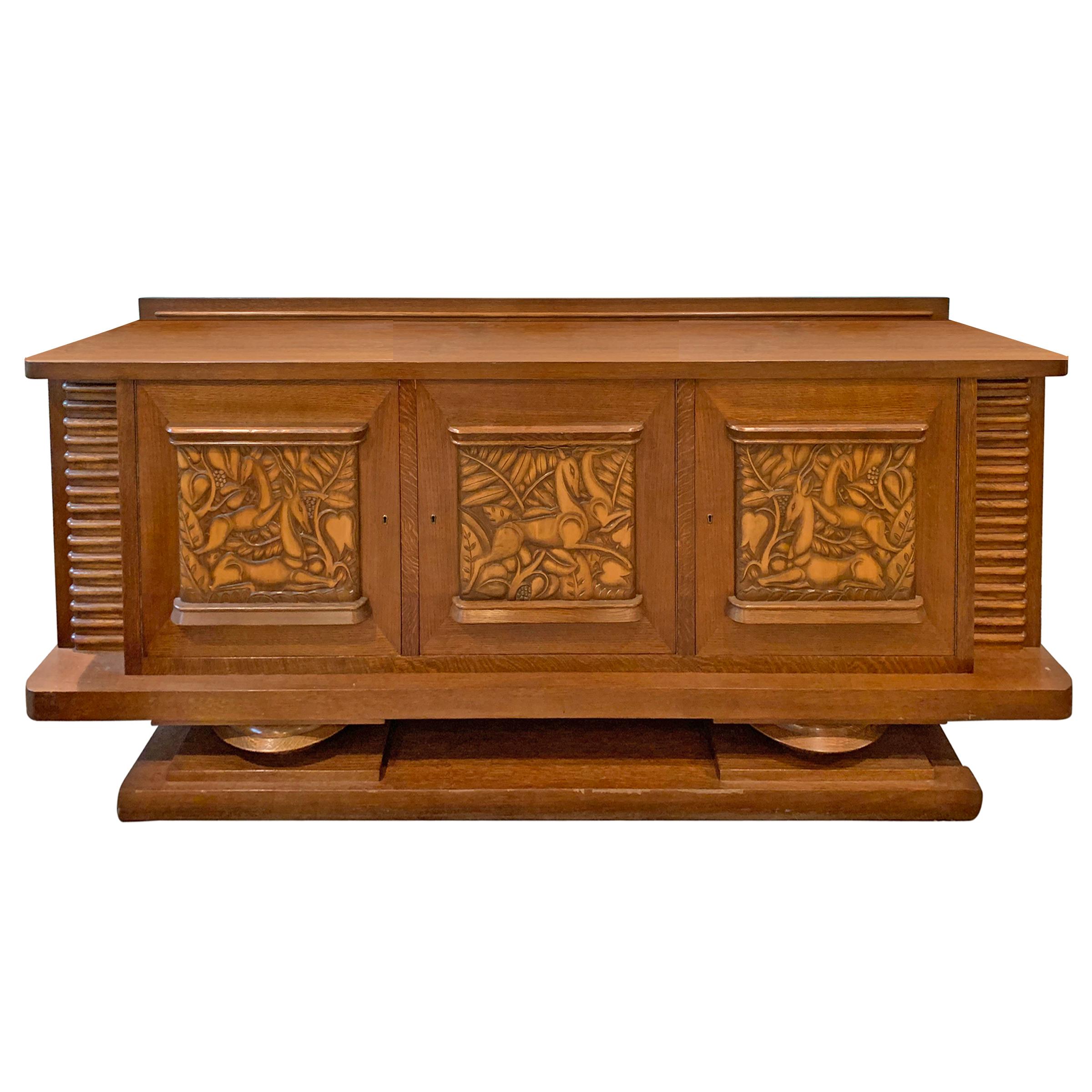 An incredible early 20th century Danish Art Deco oak cabinet with three doors, each with a classic Art Deco low relief carved antelope and palm leaf panel, large interior storage spaces, and two drawers. The entire piece rests on two wide bun feet