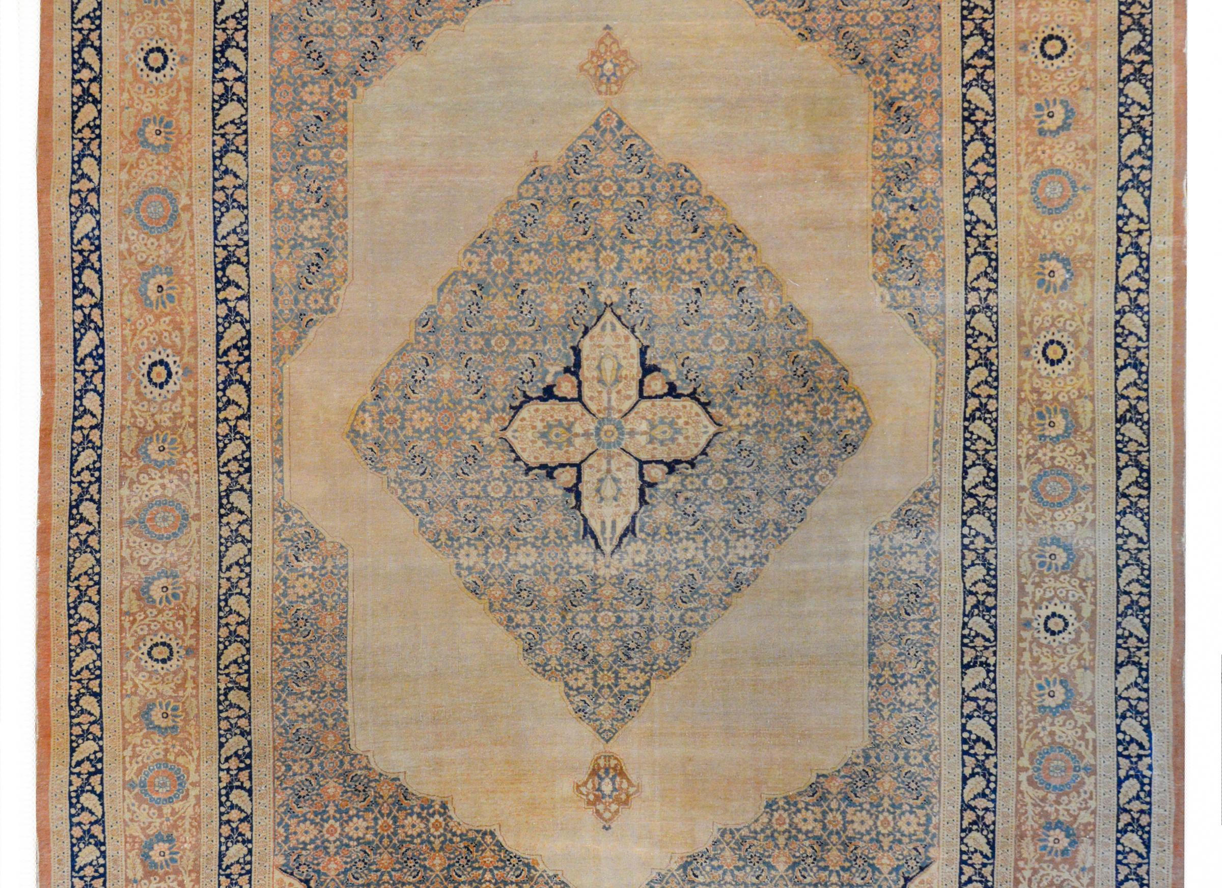 An incredible early 20th century Persian Hadji Jalili Tabriz rug with a four-lobed medallion on a larger diamond medallion with a leaf and flower trellis pattern woven in pale cream, gold, rust, and light indigo. The medallions live on an abrash
