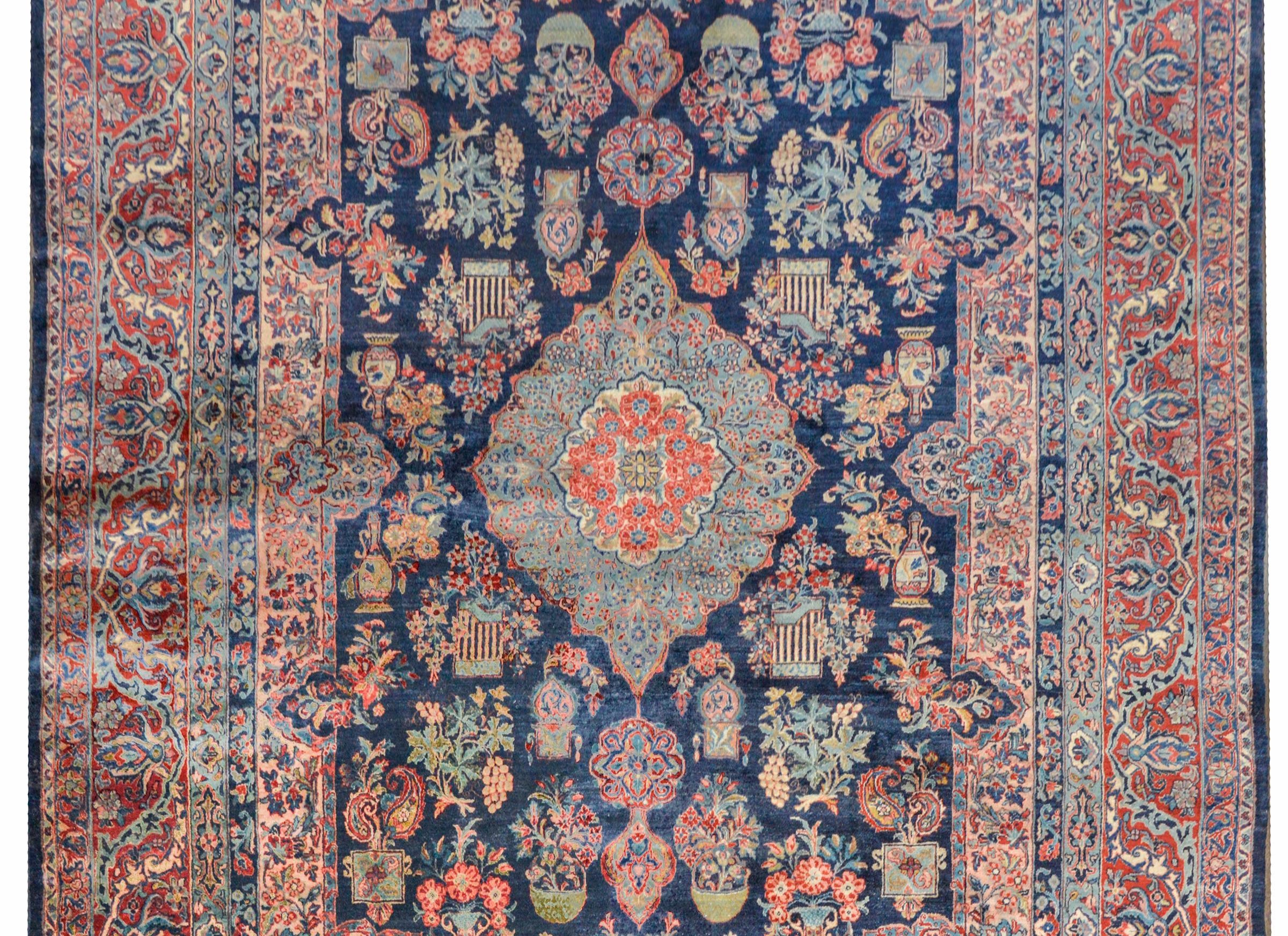An incredible early 20th century Persian Kashan rug with a fantastic pattern of myriad potted plants and flowers woven in crimson, indigo, pink, pale green, cream, and gold on a dark indigo background. The border is complex with a wide central