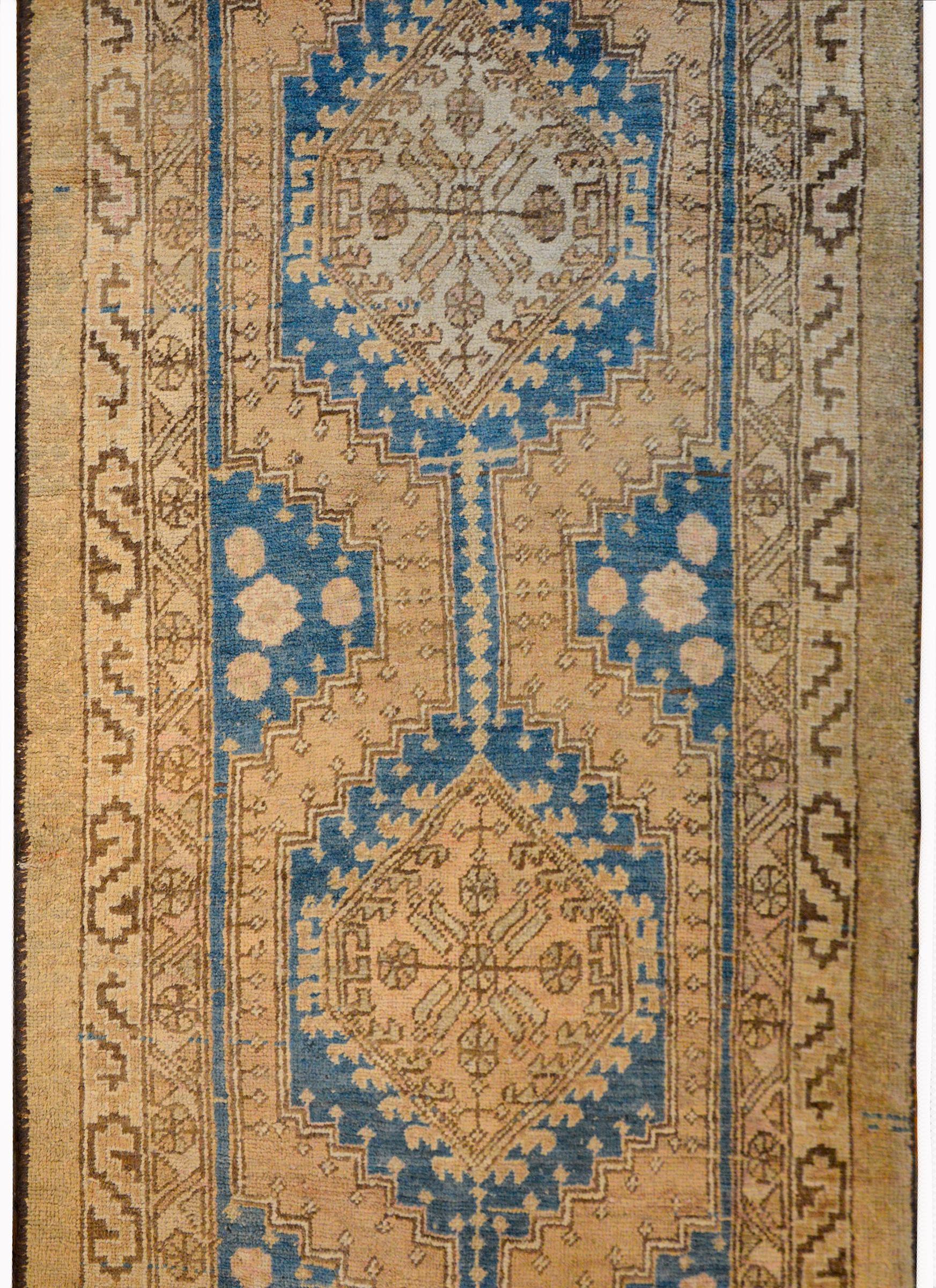 An incredible early 20th century NW Persian runner with multiple large-scale diamond medallions admits a field of stylized flowers and scrolling vines, against an Abrash indigo background turning into a natural camel colored background. The border