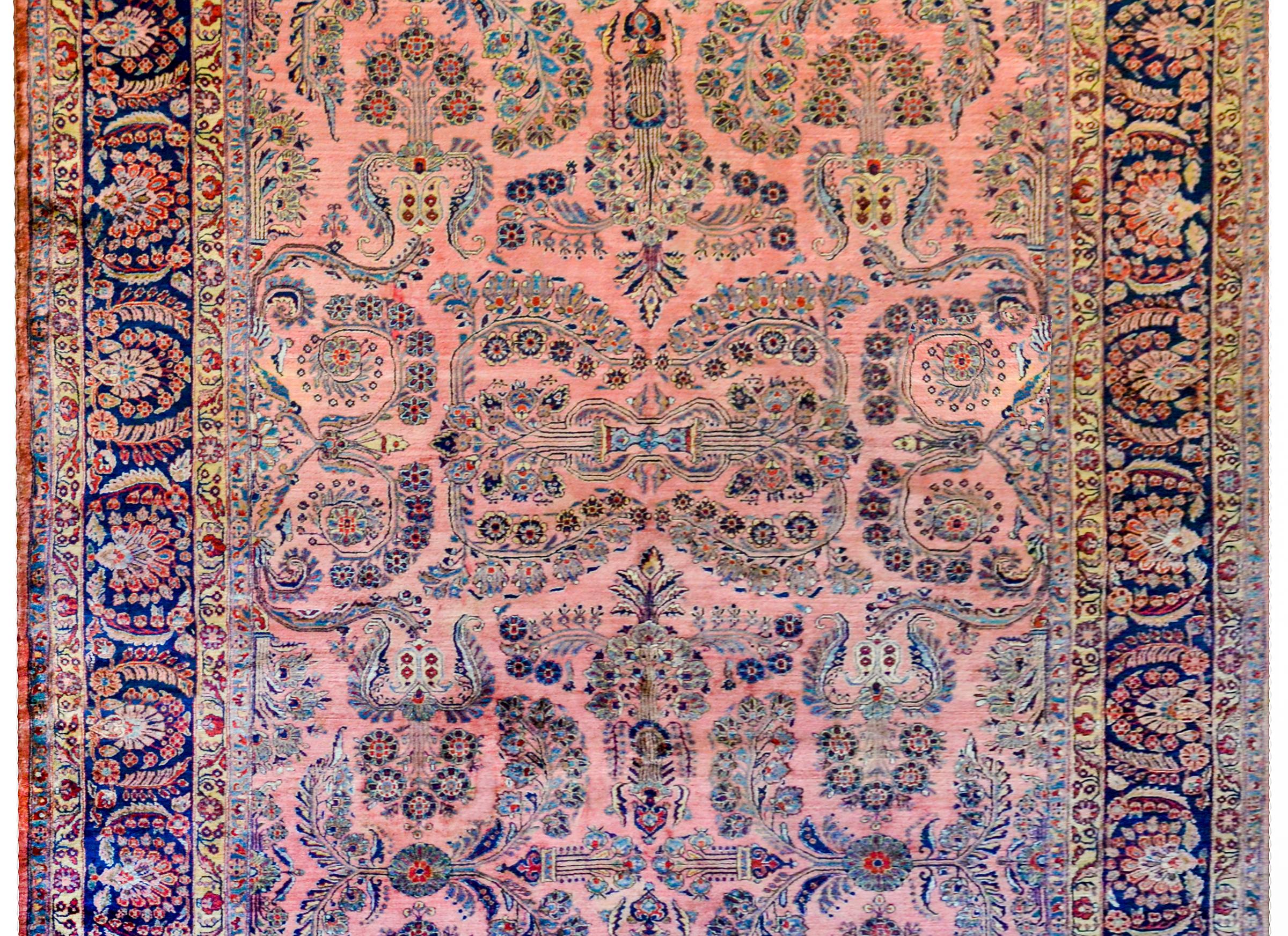 An incredible early 20th century Persian Sarouk rug with a beautiful all-over mirrored pattern of myriad flowers woven in crimson, light and dark indigo, and gold on a pale pink background. The border is outstanding with a large fanned floral