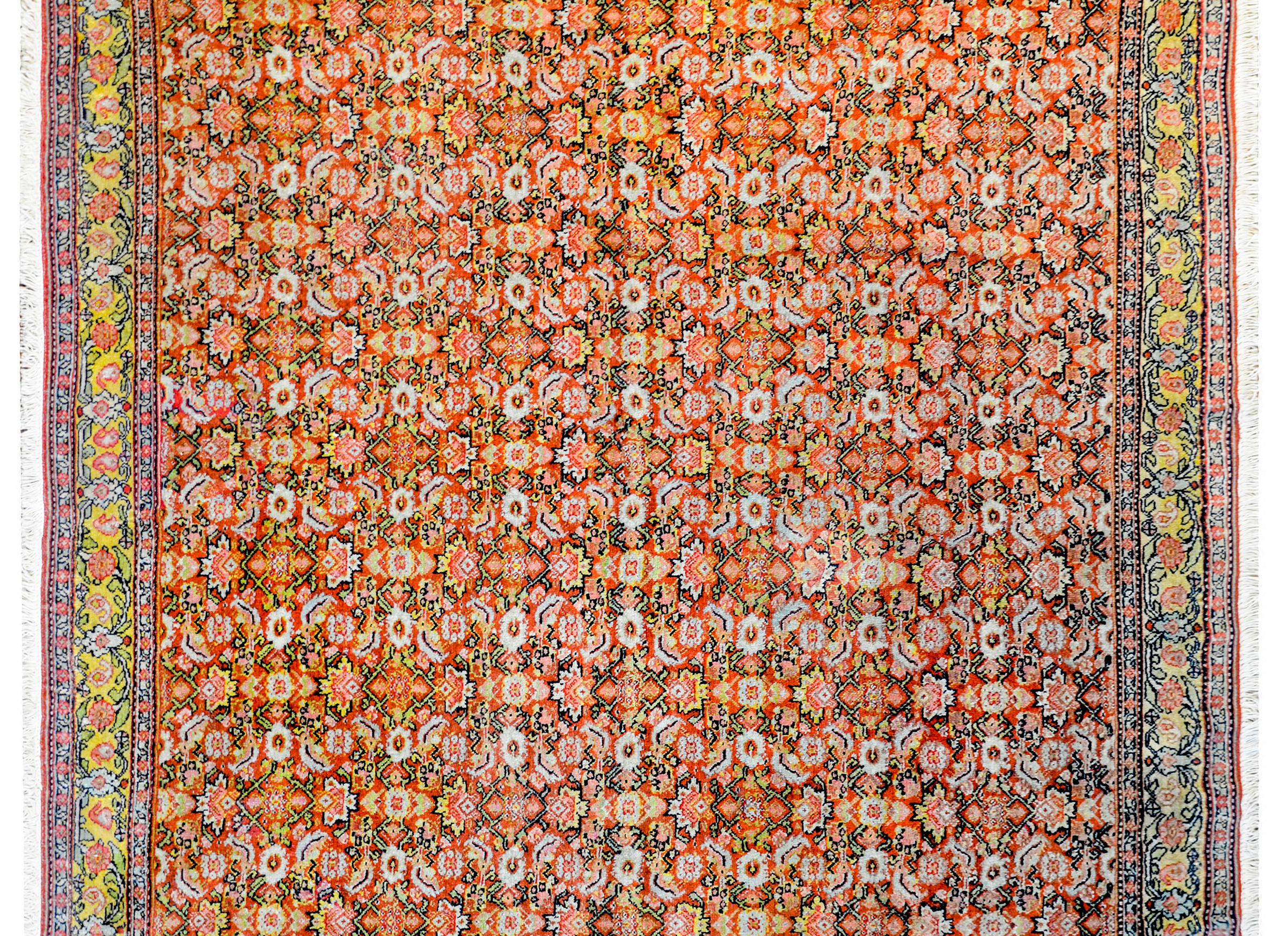 An incredible early 20th century Persian Senneh rug with an intensely woven pattern containing an all-over trellis of flowers, leaves, and vines woven in brilliant orange, gold, white, green, and black vegetable dyed wool. The border is wide with a