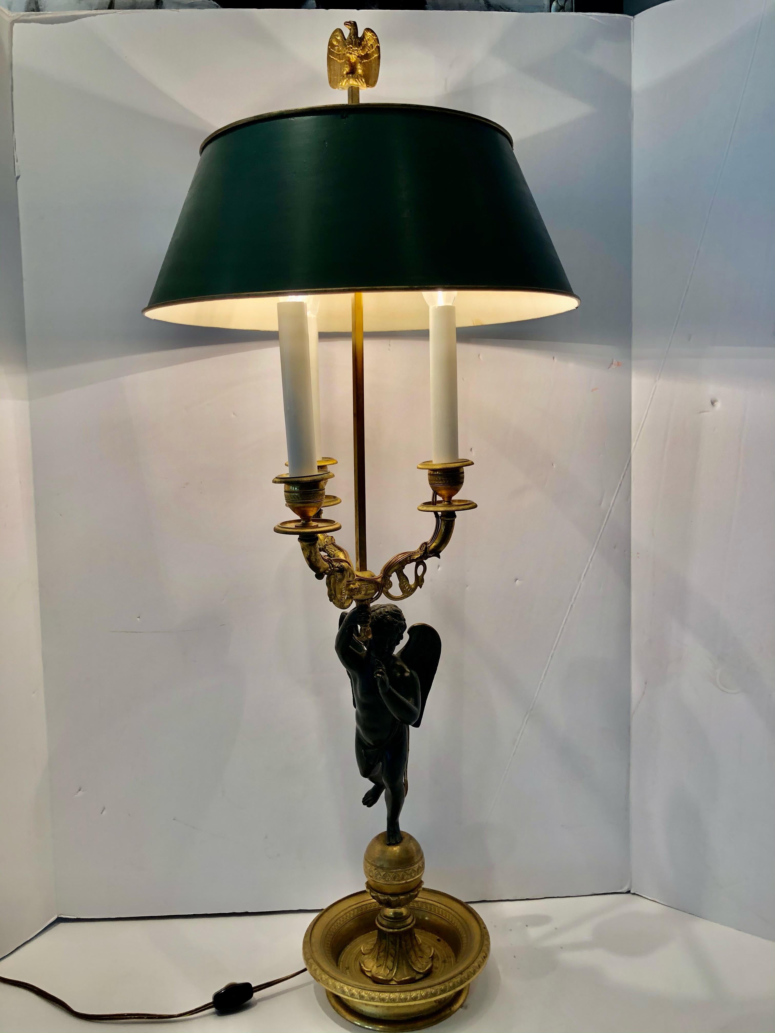 Elegant Empire style gilt bronze bouillotte lamp having embossed base with a raised spherical center. A bronze angel stands on the base supporting three lights that are decorated with swans. The green metal shade has an eagle and arrow finial and