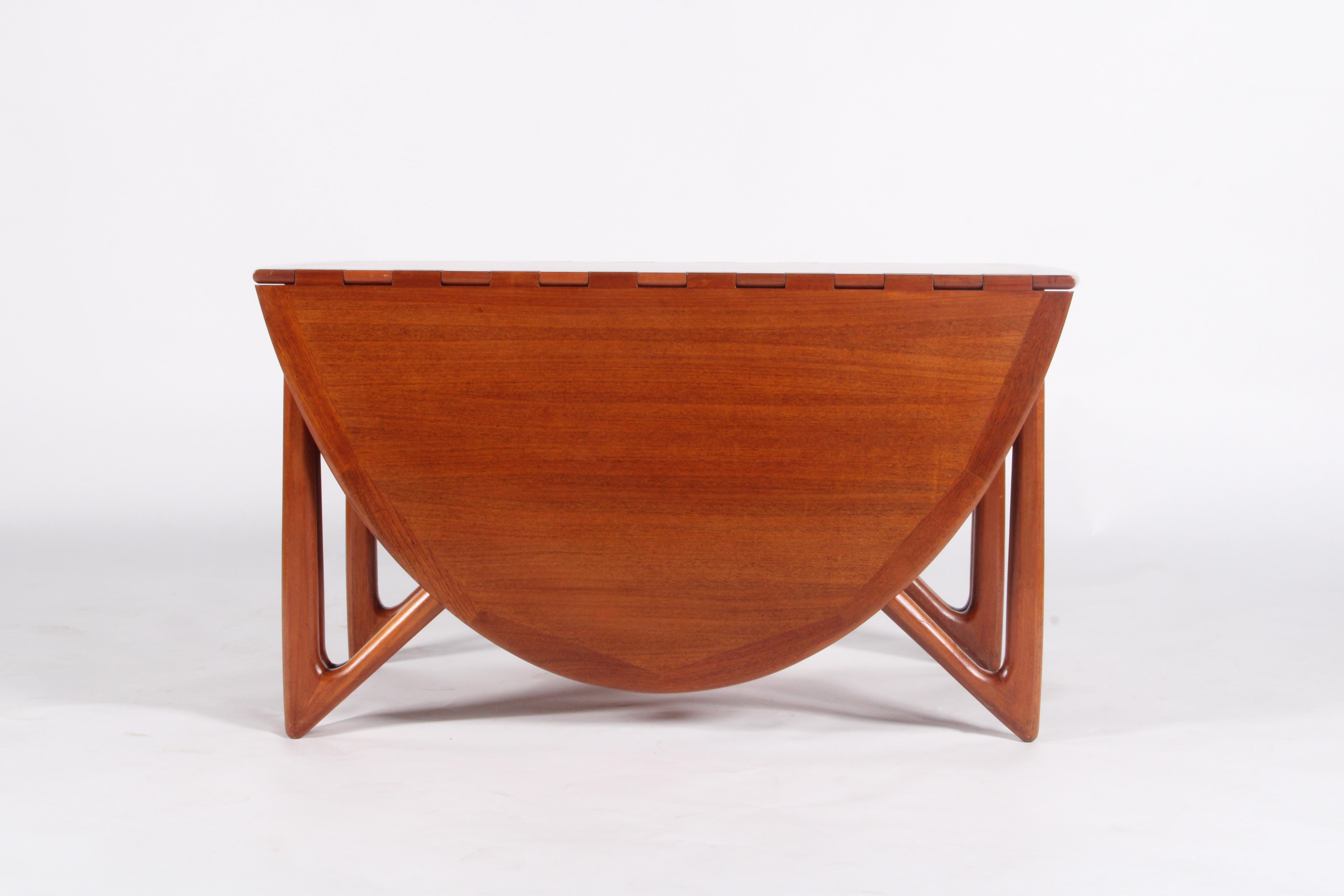 Designed by acclaimed Danish designer Niels Koefoed circa 1960, this sculptural drop-leaf dining table is a masterclass in mid-century form and function. Crafted in rich teak, it features  signature architectural base with dramatic triangulated